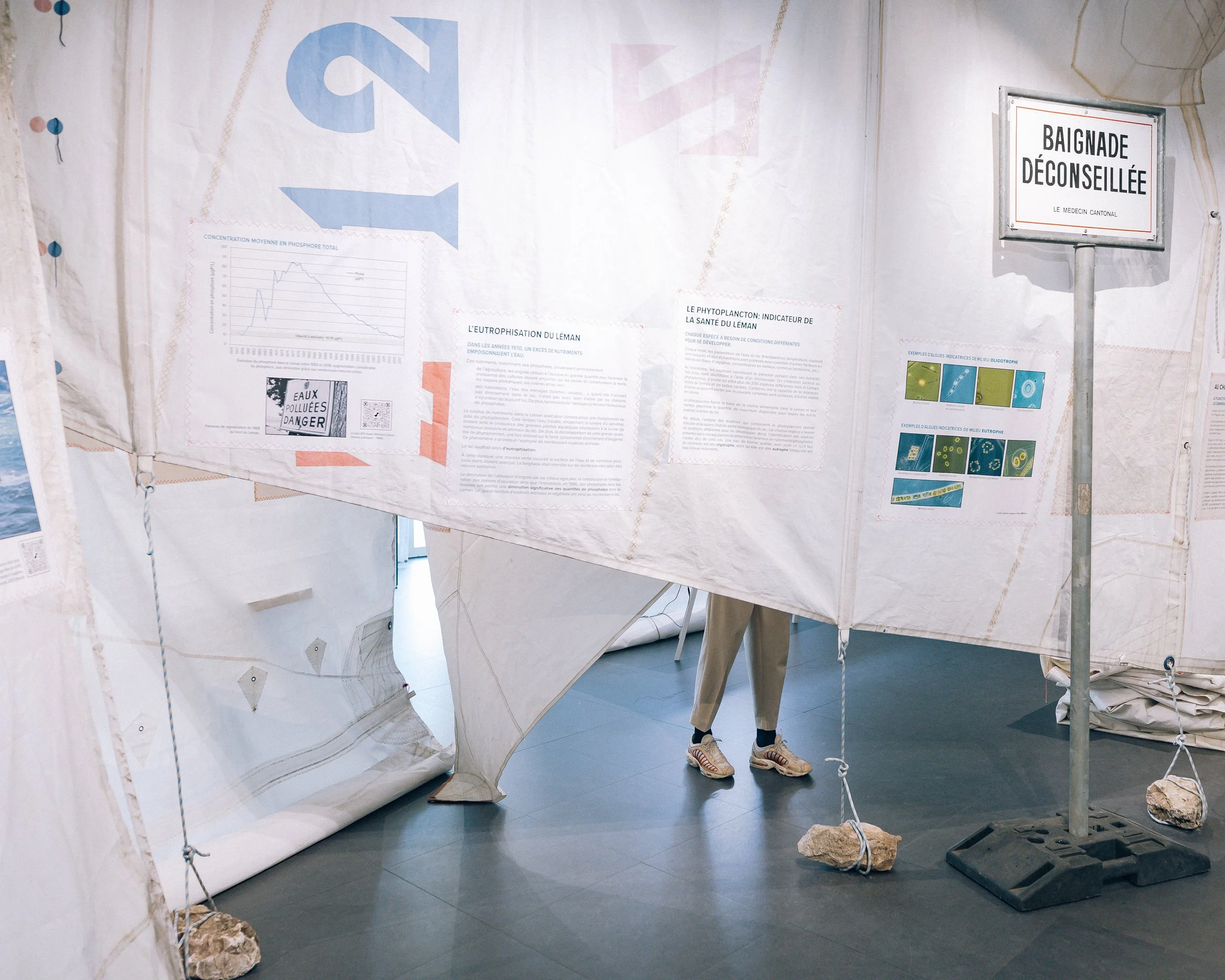 Scénographie d'exposition immersive en voiles de bateaux dans un musée avec affiches, objets et panneaux d'information sur le thème du plancton. On voit les jambes d'un visiteur de l'exposition dépasser.
