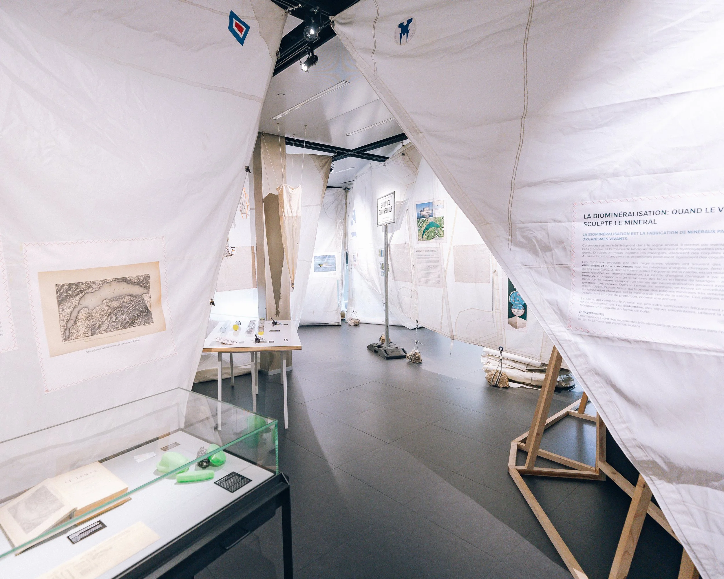 Une exposition dans un musée avec des affiches et objets historiques, principalement entourée de paravents en tissu blanc.