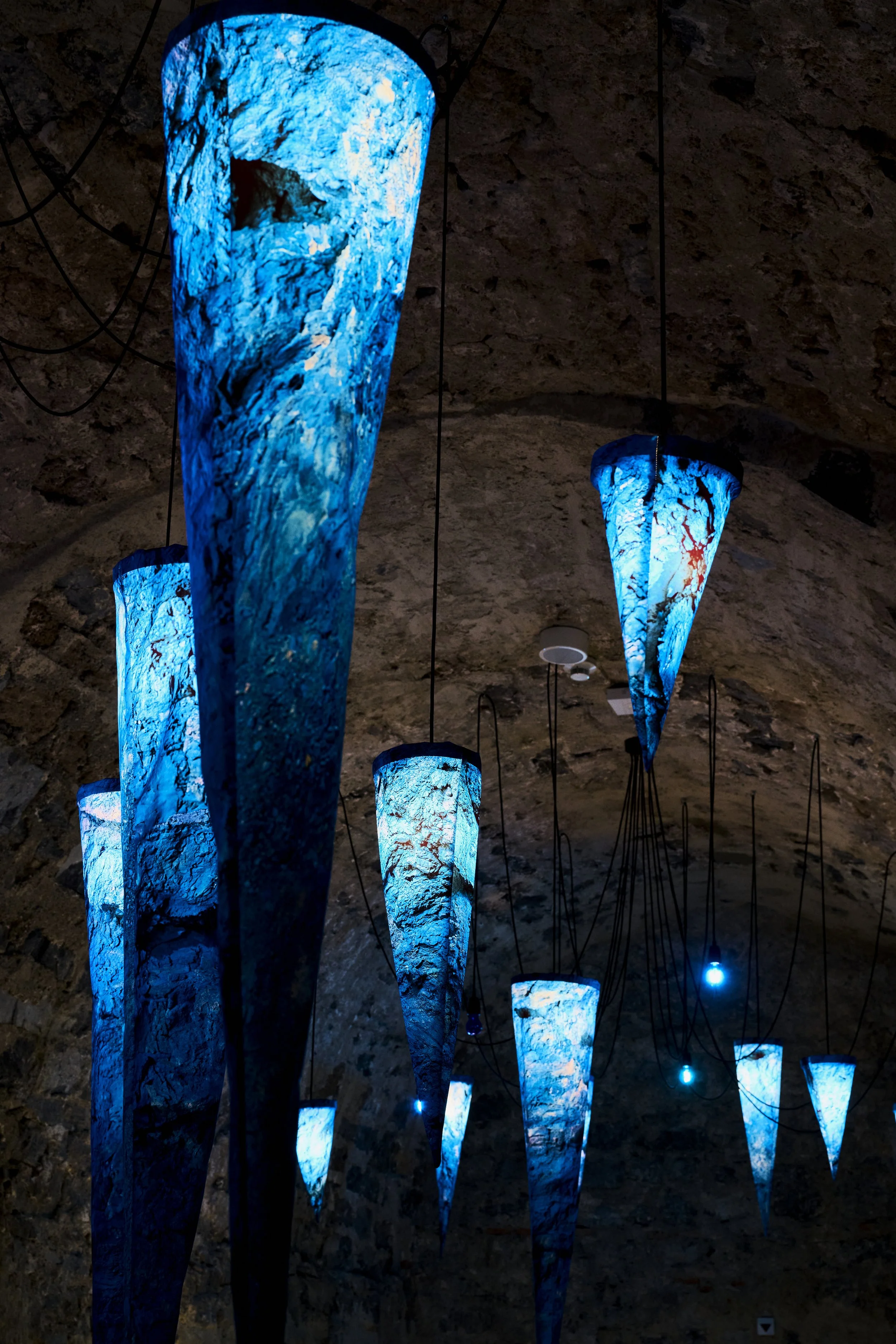 Luminaires suspendus en forme de fleurs bleues avec des motifs marbrés, éclairant une surface rocheuse ou un plafond en intérieur.