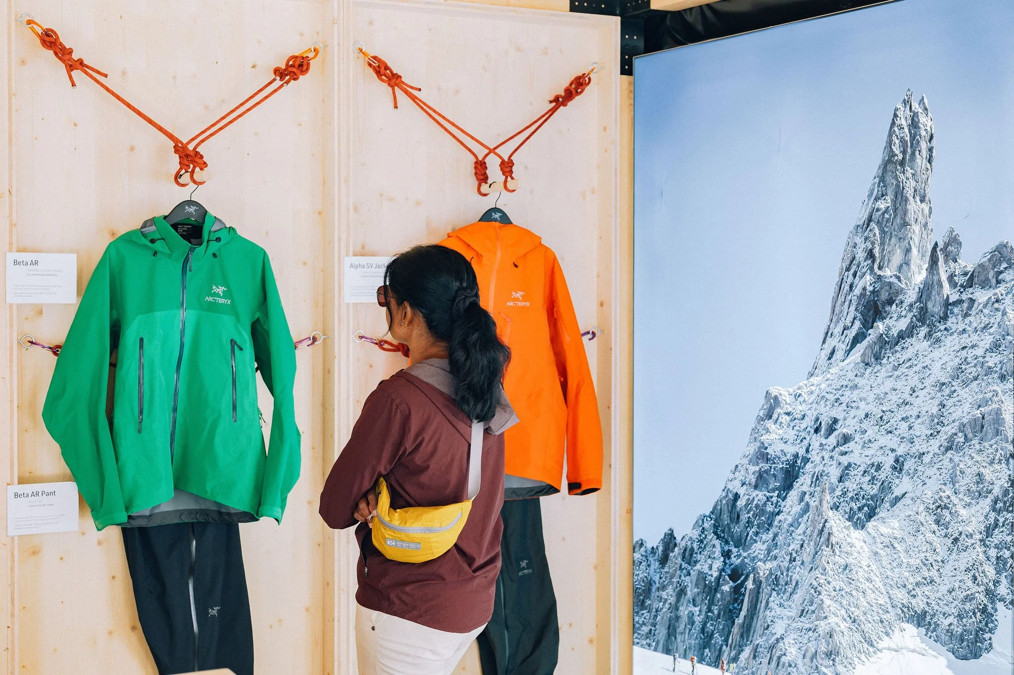 Vêtements d'extérieur pour l'alpinisme exposés dans un magasin, avec une montagne enneigée en fond.