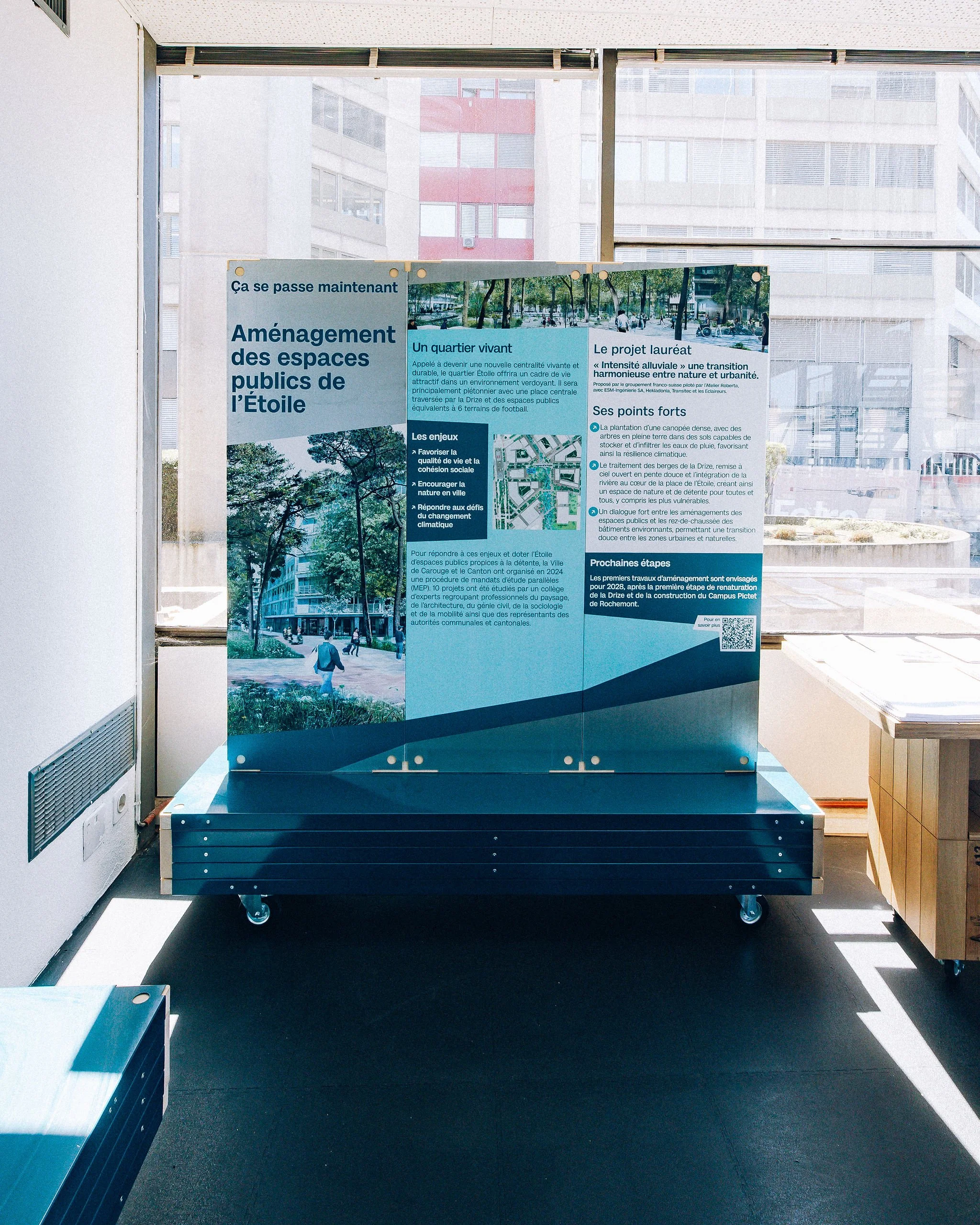 Scénographie d'exposition du projet urbanistique Praille Acacias Vernet à Genève. Affiche d'informations sur l'aménagement des espaces publics de l'Étoile, comprenant du texte et des images de quartiers et espaces verts.