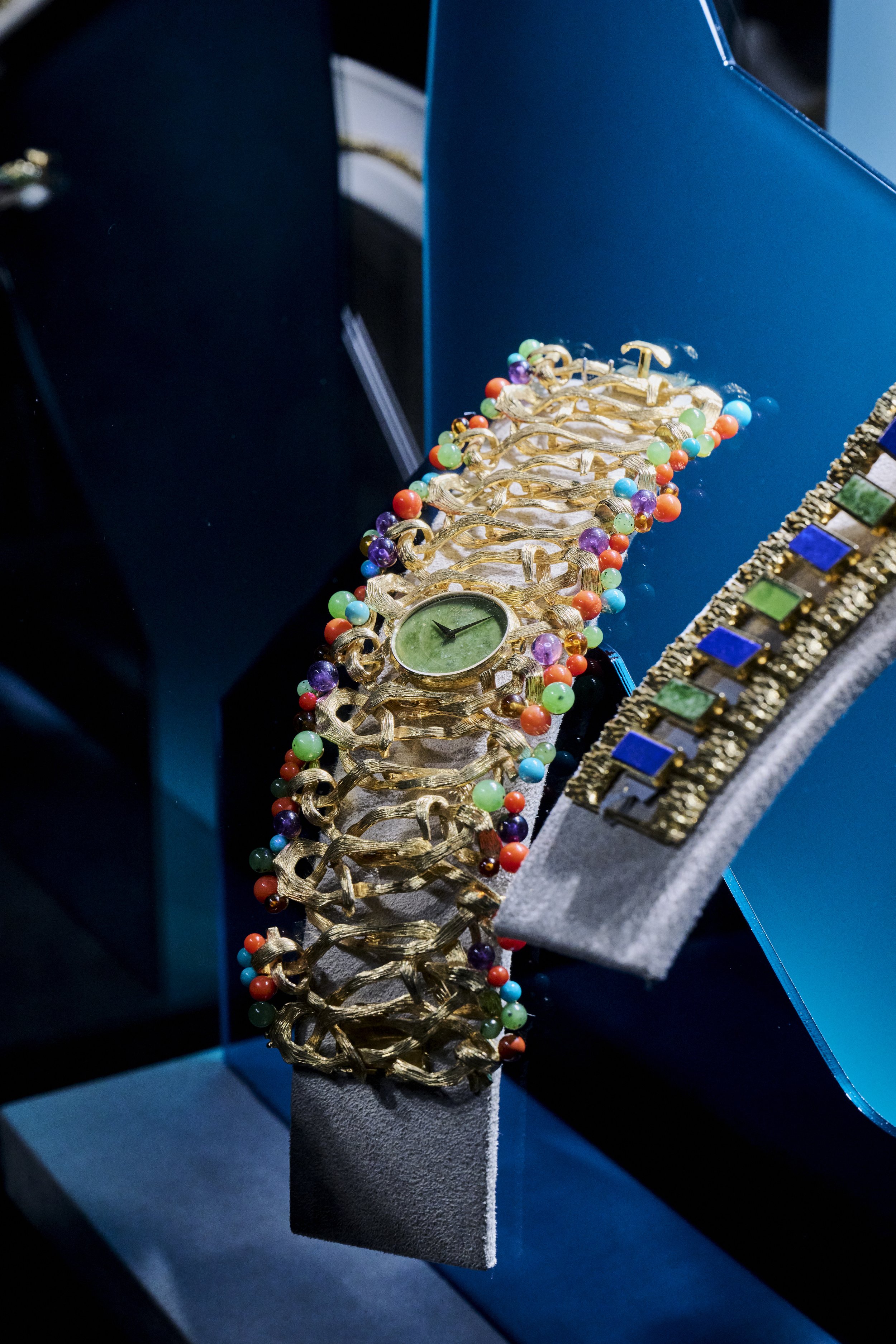 Une montre en or avec un bracelet décoré de perles de différentes couleurs, exposée sur un support dans une vitrine.