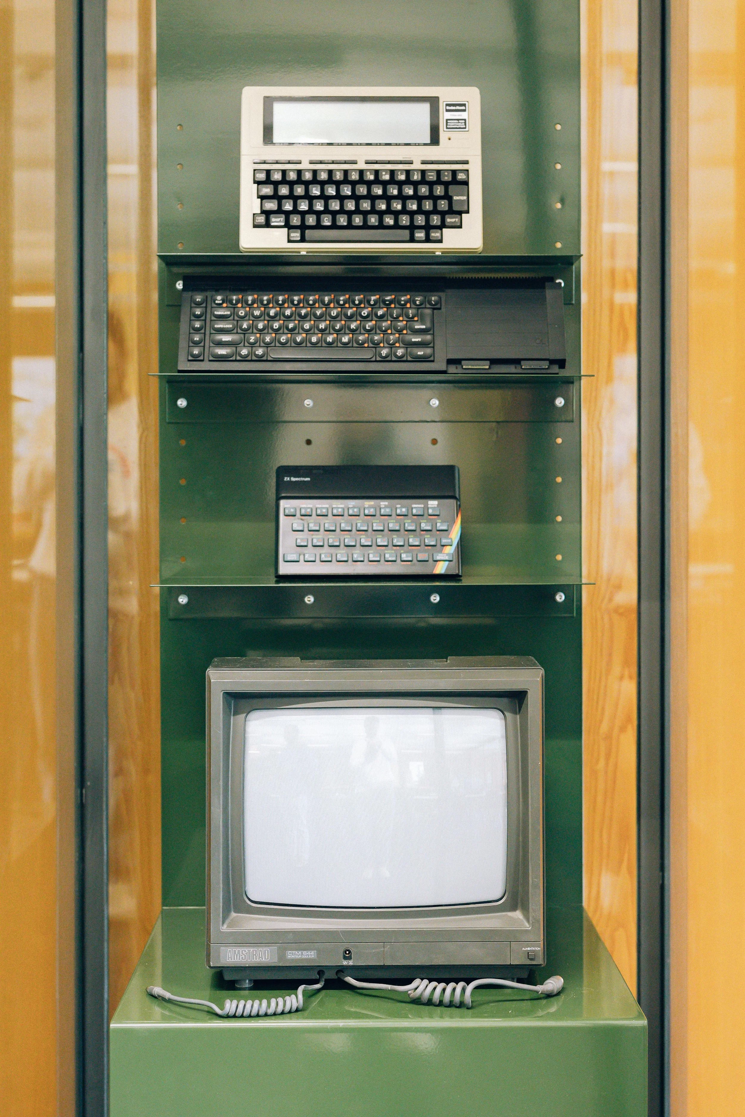 Une vitrine contenant une console de jeux vintage, deux autres appareils électroniques et un vieux téléviseur CRT.