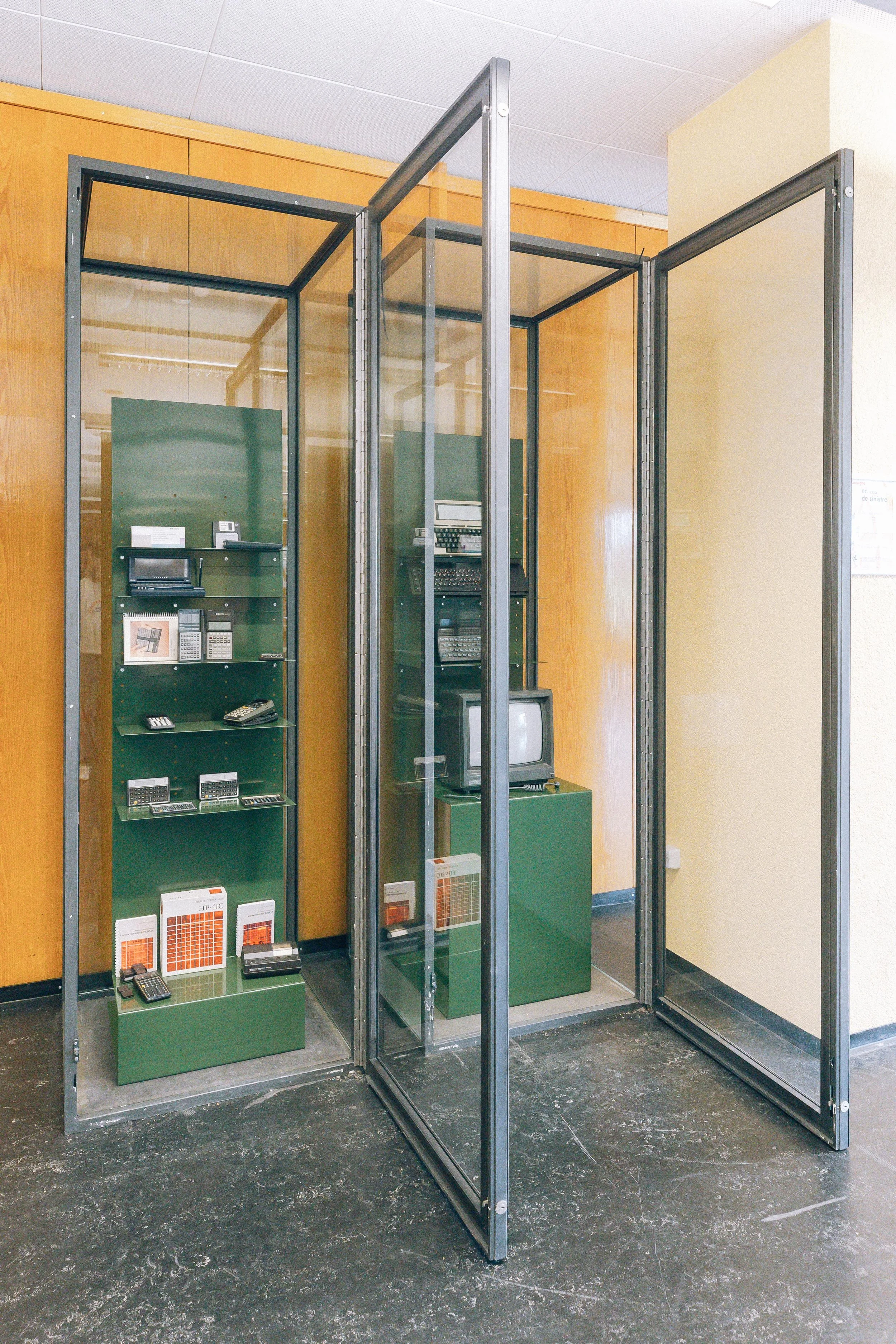 Une cabine d'information ou de sécurité avec des appareils électroniques et des éléments de chauffage, entourée d'un cadre en métal, située dans un bâtiment avec murs en bois et plafond en dalles blanches.