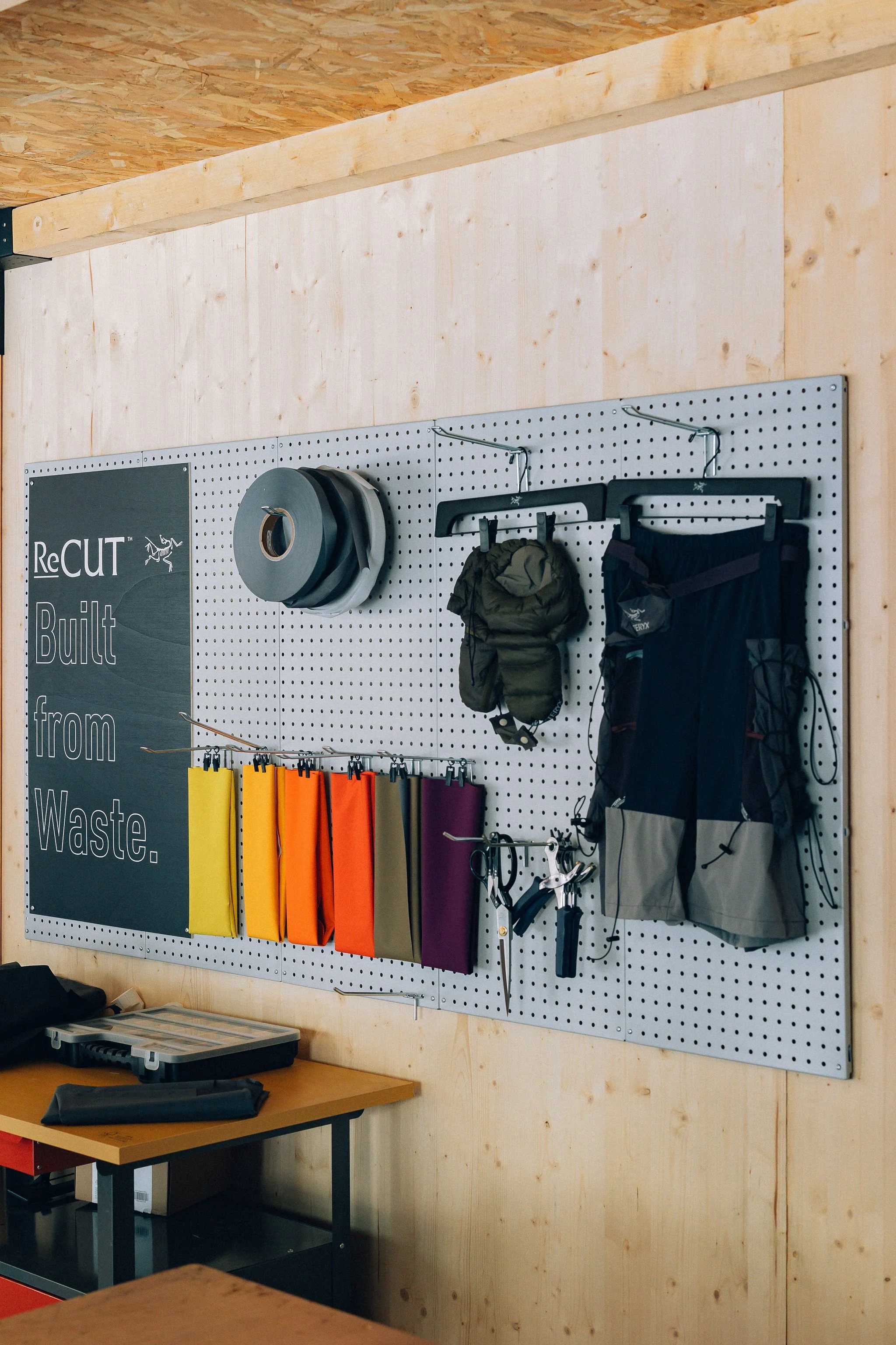 Mur de workshop avec matériel de camping et outils, affiche avec texte 'ReCUT Built from Waste', étagère, et table de travail.