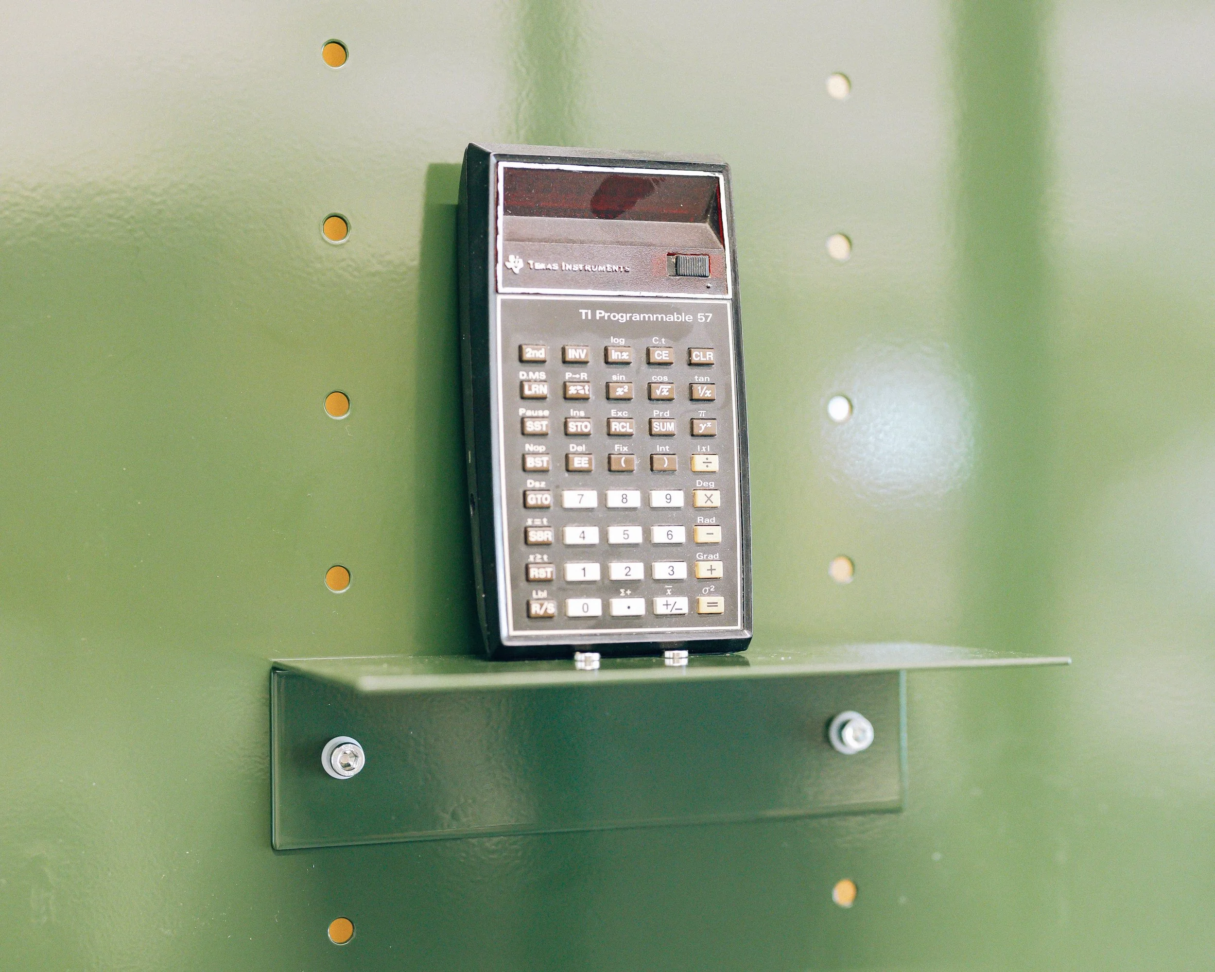 Une calculatrice scientifique TI Programmable 57 fixée sur un panneau vert avec des vis.