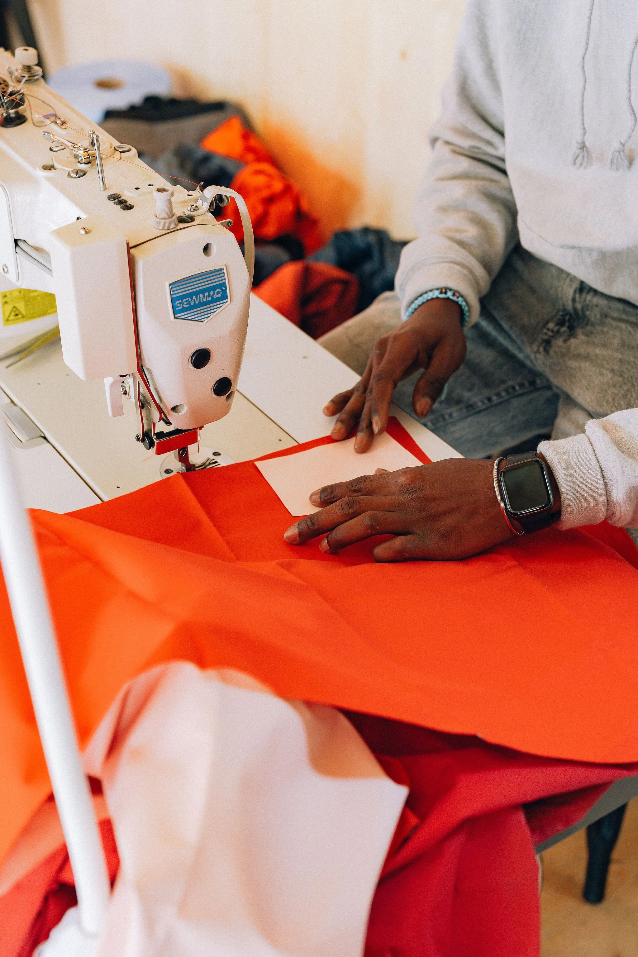 Une personne utilisant une machine à coudre blanche pour coudre du tissu orange.