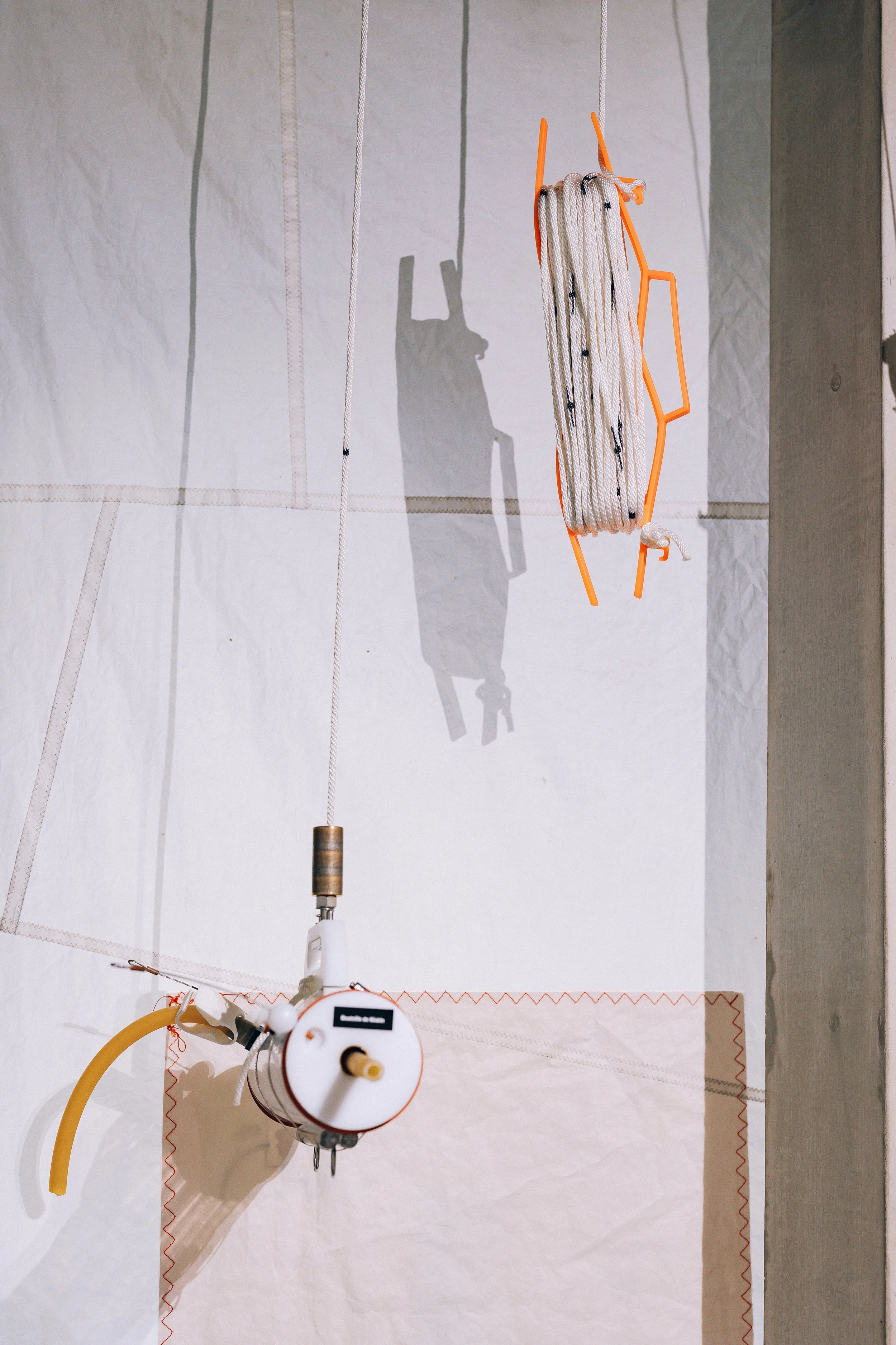 Dispositif scientifique avec tuyaux, cadran et structure en plastique orange, suspendu devant des voiles de bateau au sein d'une exposition scientifique.