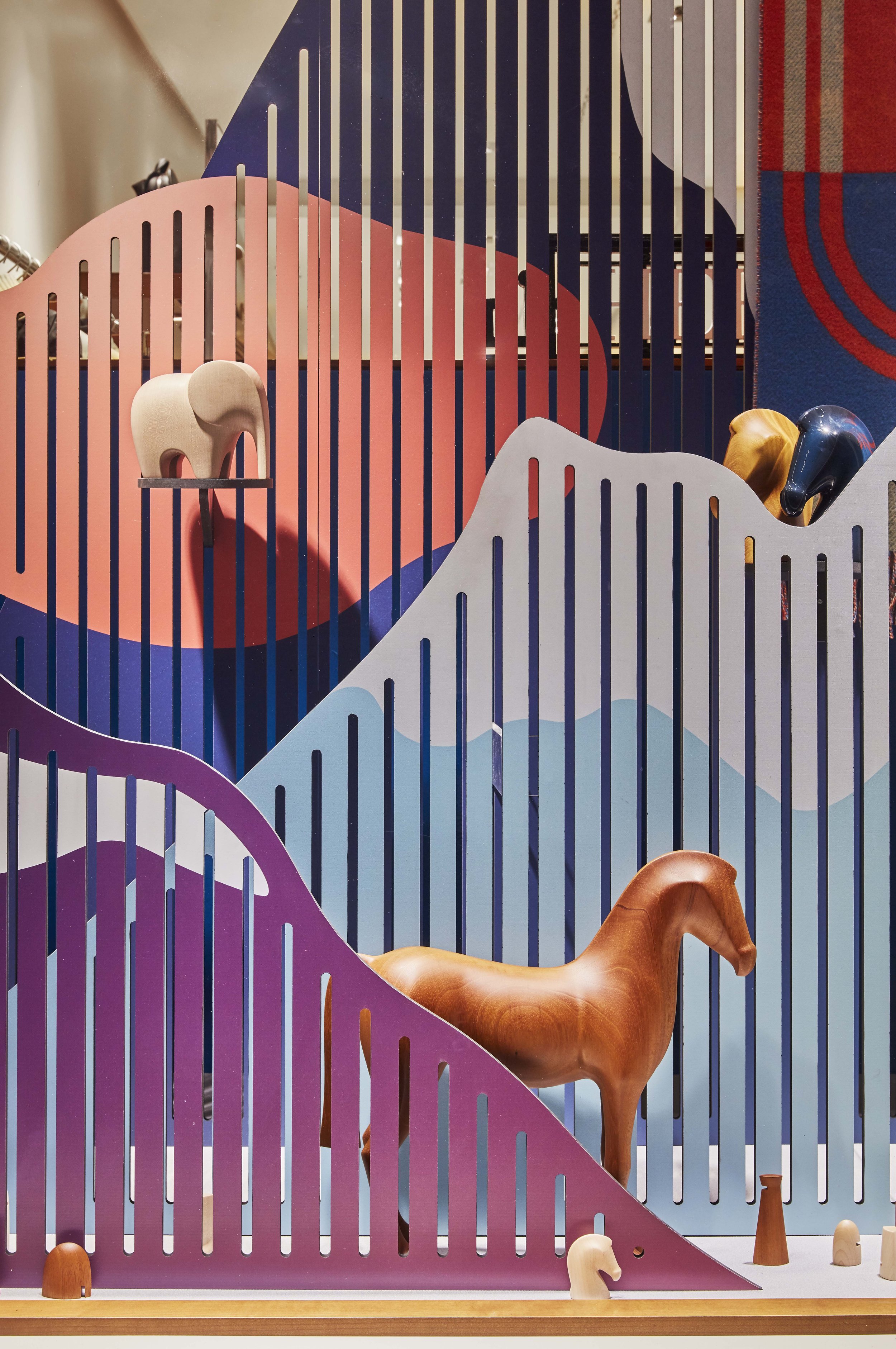 Scénographie de vitrines du magasin Hermès Genève représentant un paysage de montagne en Suisse et mettant en valeur des objets de décoration Hermès en forme d'animaux en bois comme un cheval et un éléphant.