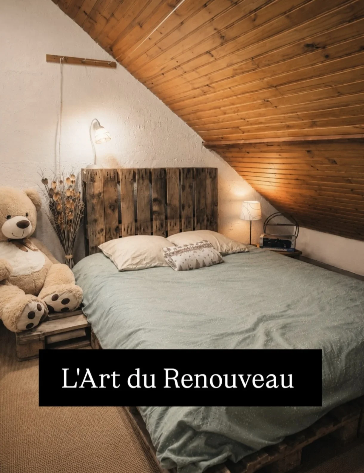 Chambre avec un lit en bois, un ours en peluche à côté, lampes de chevet, et un motif floral sur les coussins, sous un plafond en bois incliné.