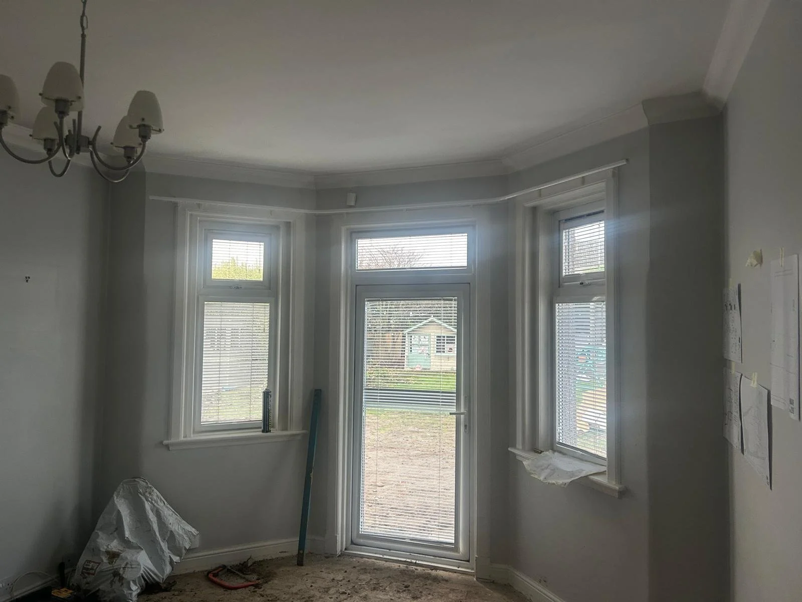 Interior room with three large windows and one glass door, white walls, crown molding, a chandelier light fixture, and construction materials on the floor.