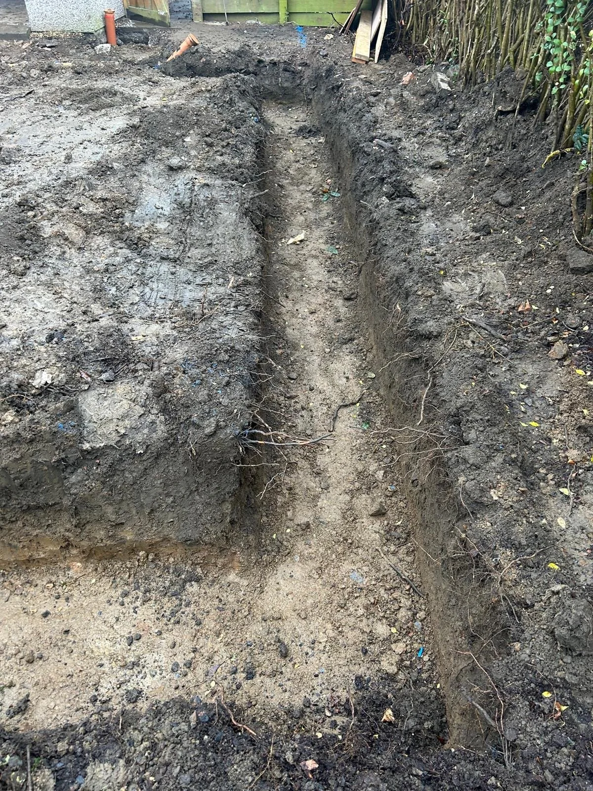 A narrow trench dug in the soil in a garden or backyard, with dirt piled on either side.