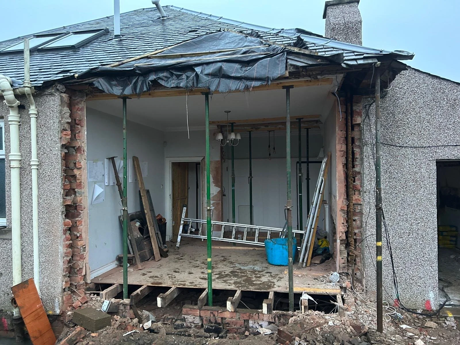 House under renovation with hole in the wall, construction tools, and scaffolding inside, exposing the interior room.