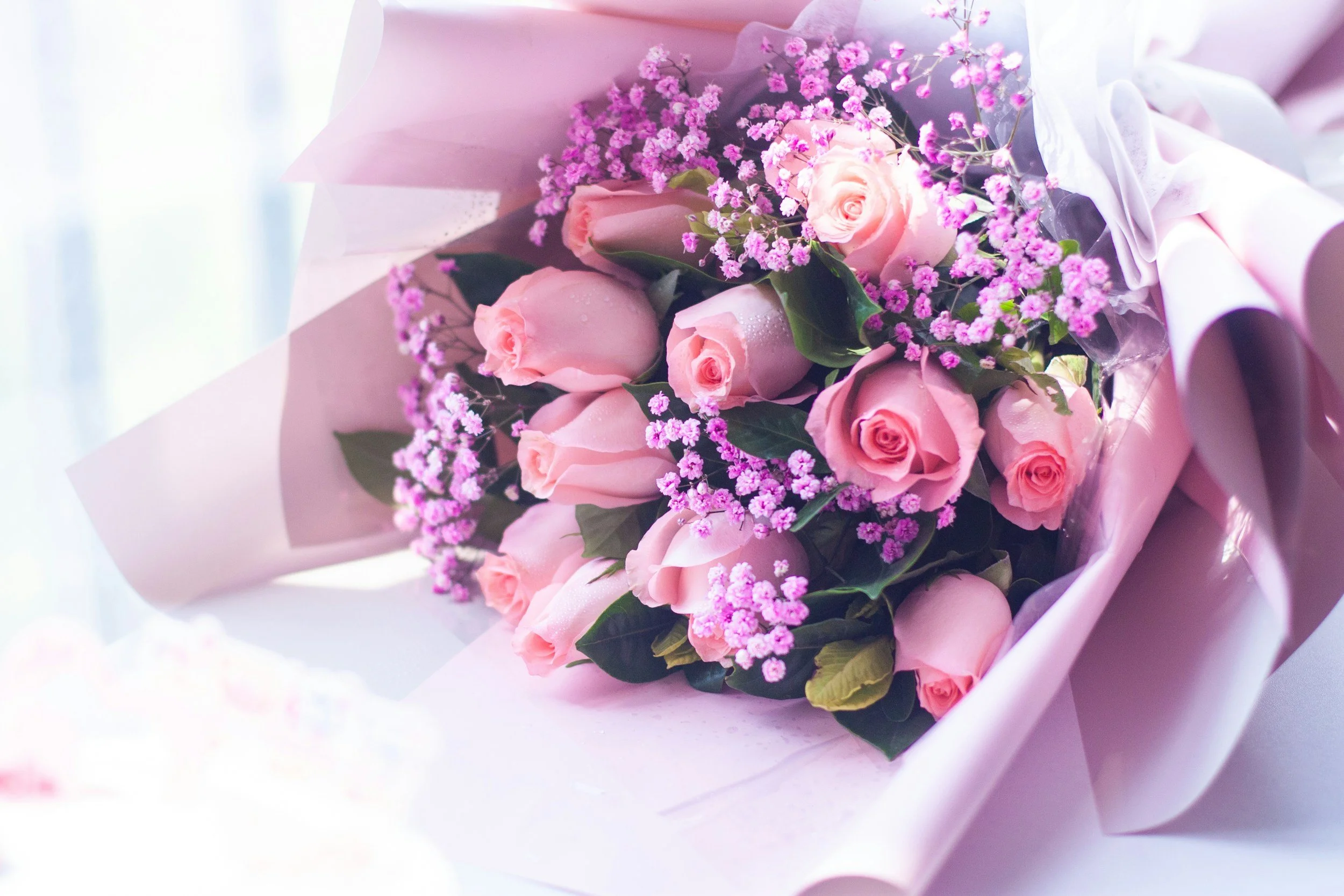 A bouquet of pink roses and purple baby's breath flowers wrapped in pink paper.