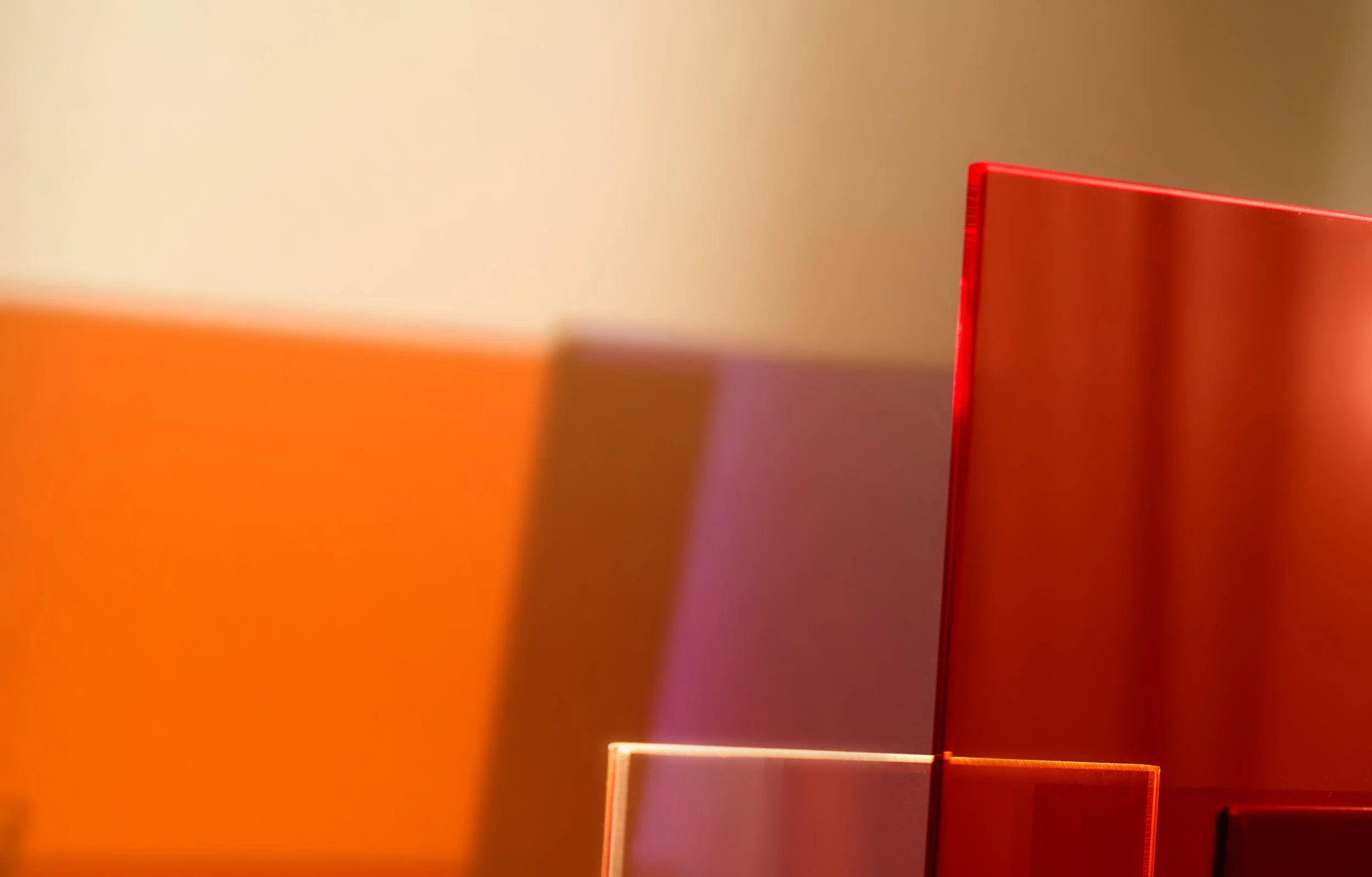 Designerlampe in Rot- und Orangetönen, die ein warmes, farbiges Schattenspiel auf die Wand dahinter wirft.