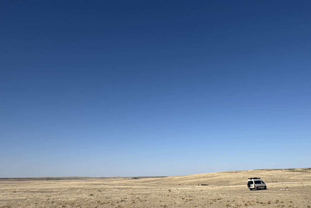 A CNA camper van parked in a vast, open desert landscape under a clear, bright blue sky.  West Texas, New Mexico.  Wide open spaces.  Boon docking camper van.  Boon docking. Camper van.