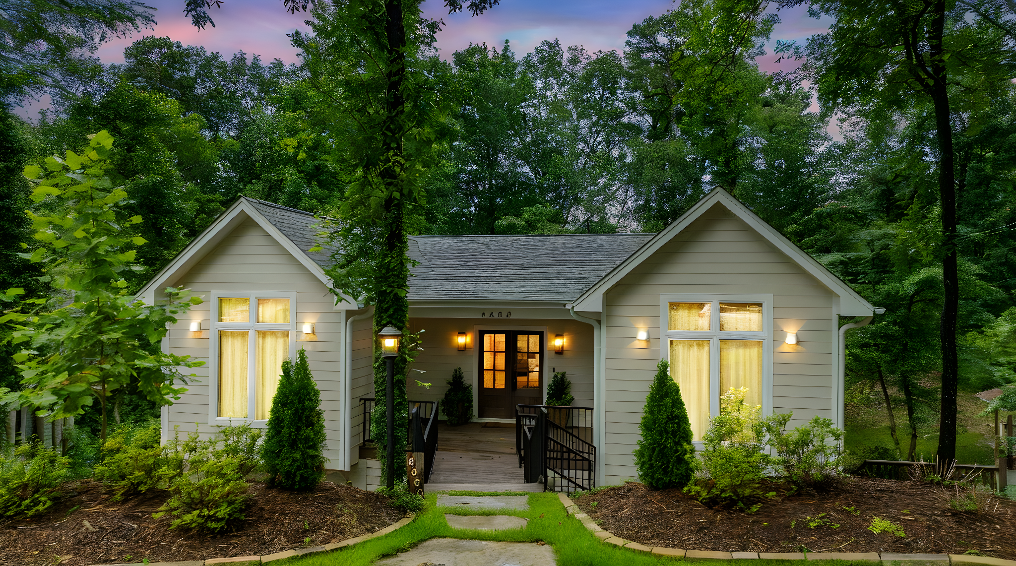 A cozy house surrounded by lush green trees at twilight, with warm yellow lighting visible in the windows and front porch area.