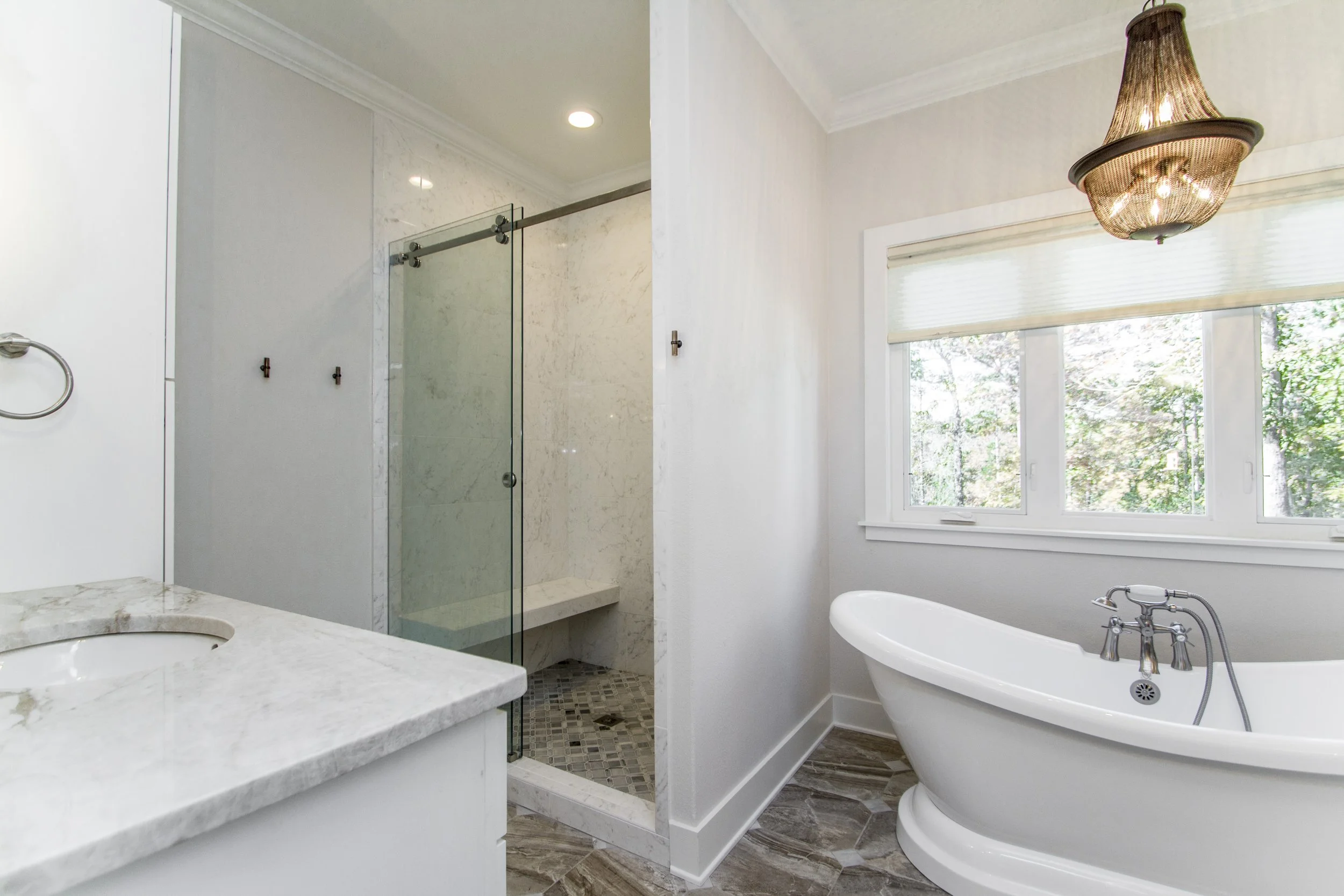 A bathroom with a marble vanity, a glass-enclosed shower, a clawfoot bathtub, a window with blinds, and a decorative ceiling light fixture.