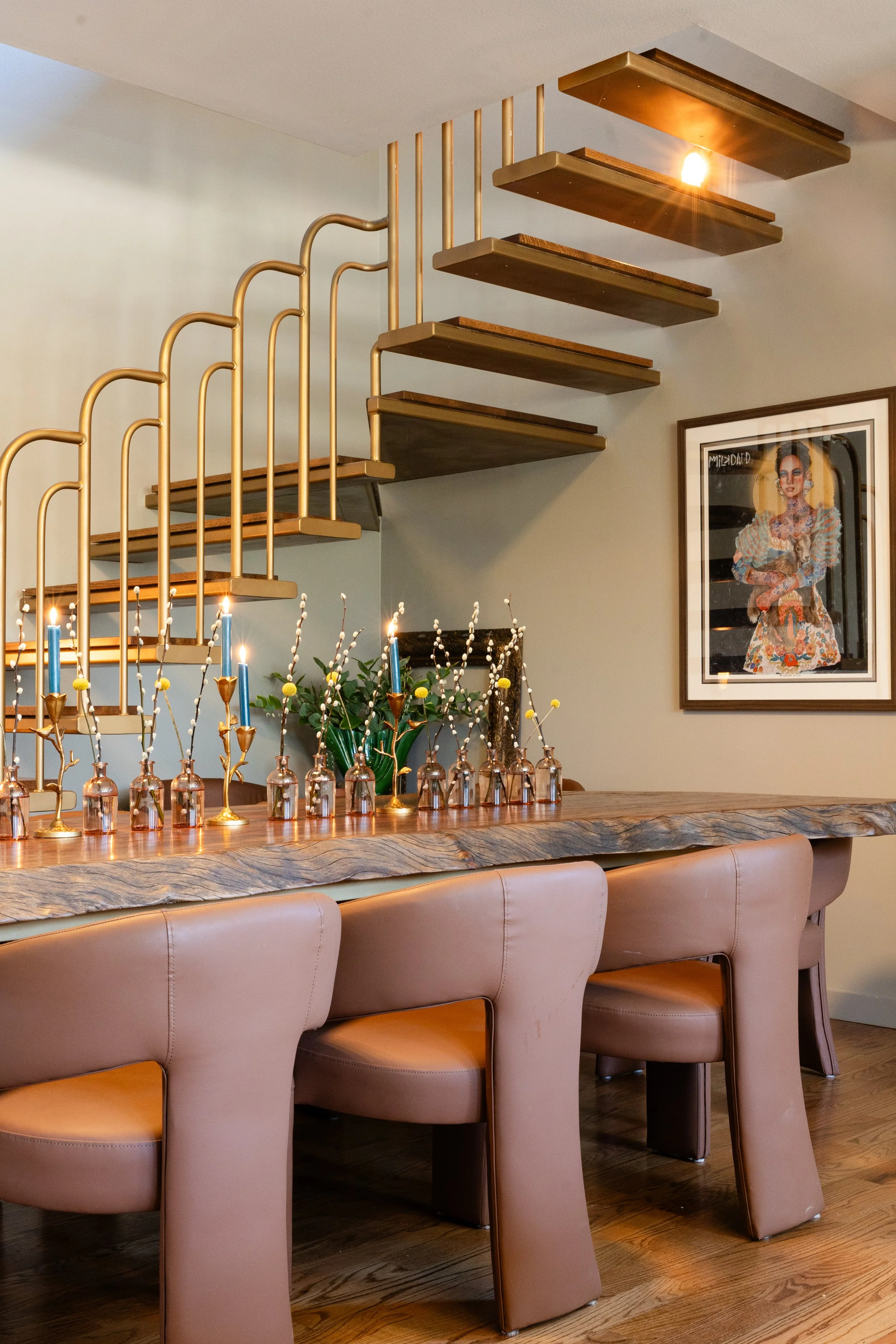 Interior of a modern dining area with a wooden counter, pink chairs, decorative flowers, and a framed artwork of a woman on the wall.