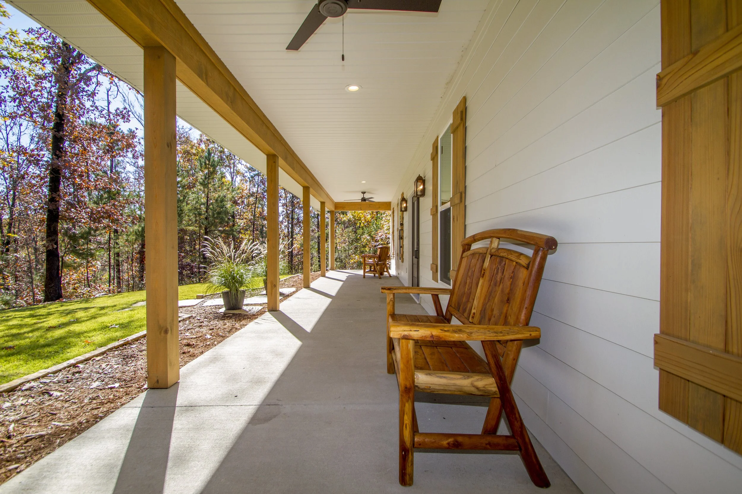 Front porch of a house with wooden bench seats and a view of trees with autumn foliage.