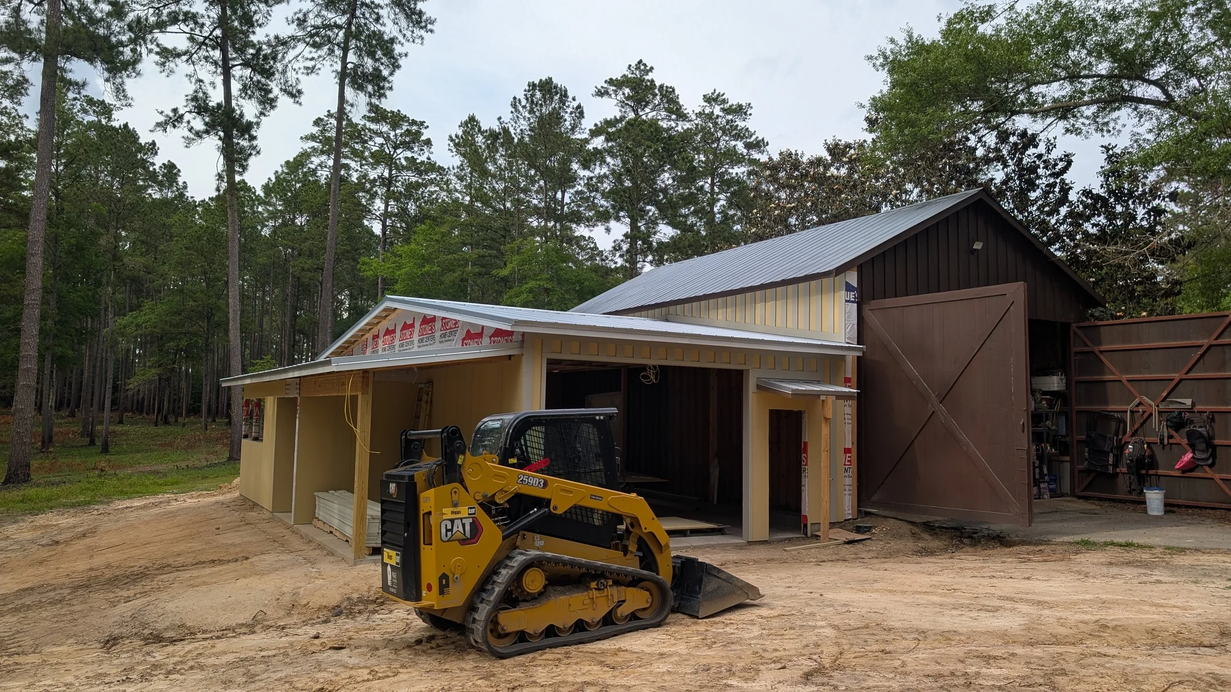 Construction site with partially built garage, construction equipment, and surrounding forested area.