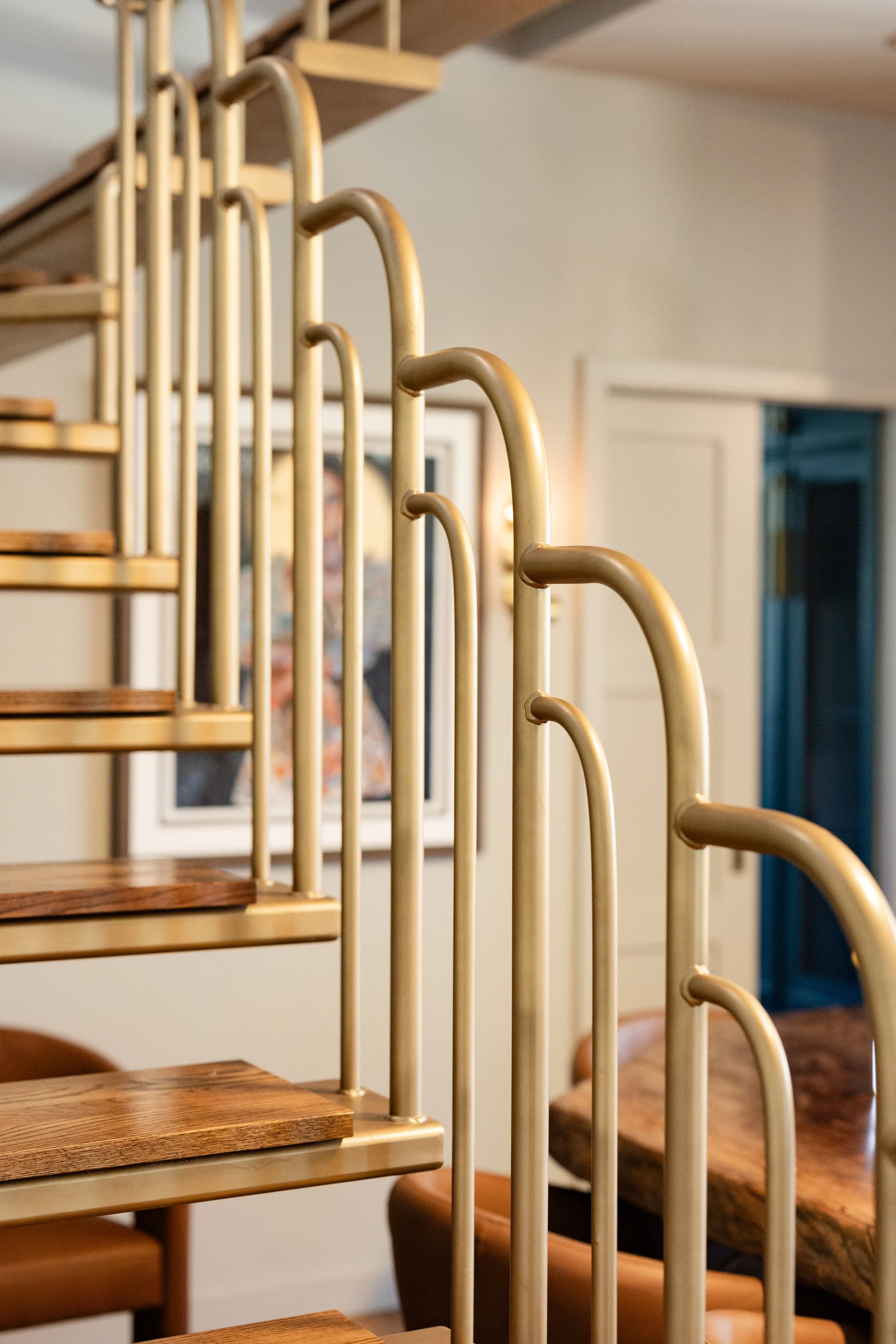 Close-up of a staircase with wooden steps and cream-colored metal railings in a cozy indoor setting, with a blurred background showing parts of a person and a hallway.