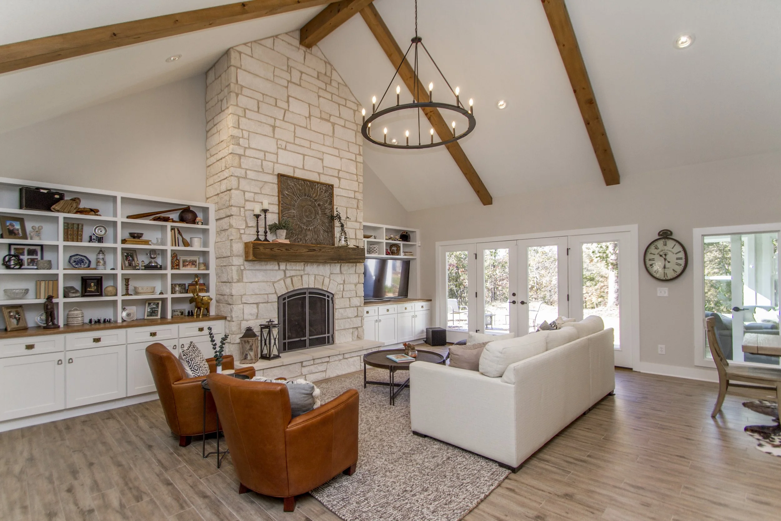 Living room with beige sofa, brown rocking chairs, white shelves with decor, a stone fireplace, and a chandelier hanging from a vaulted ceiling.