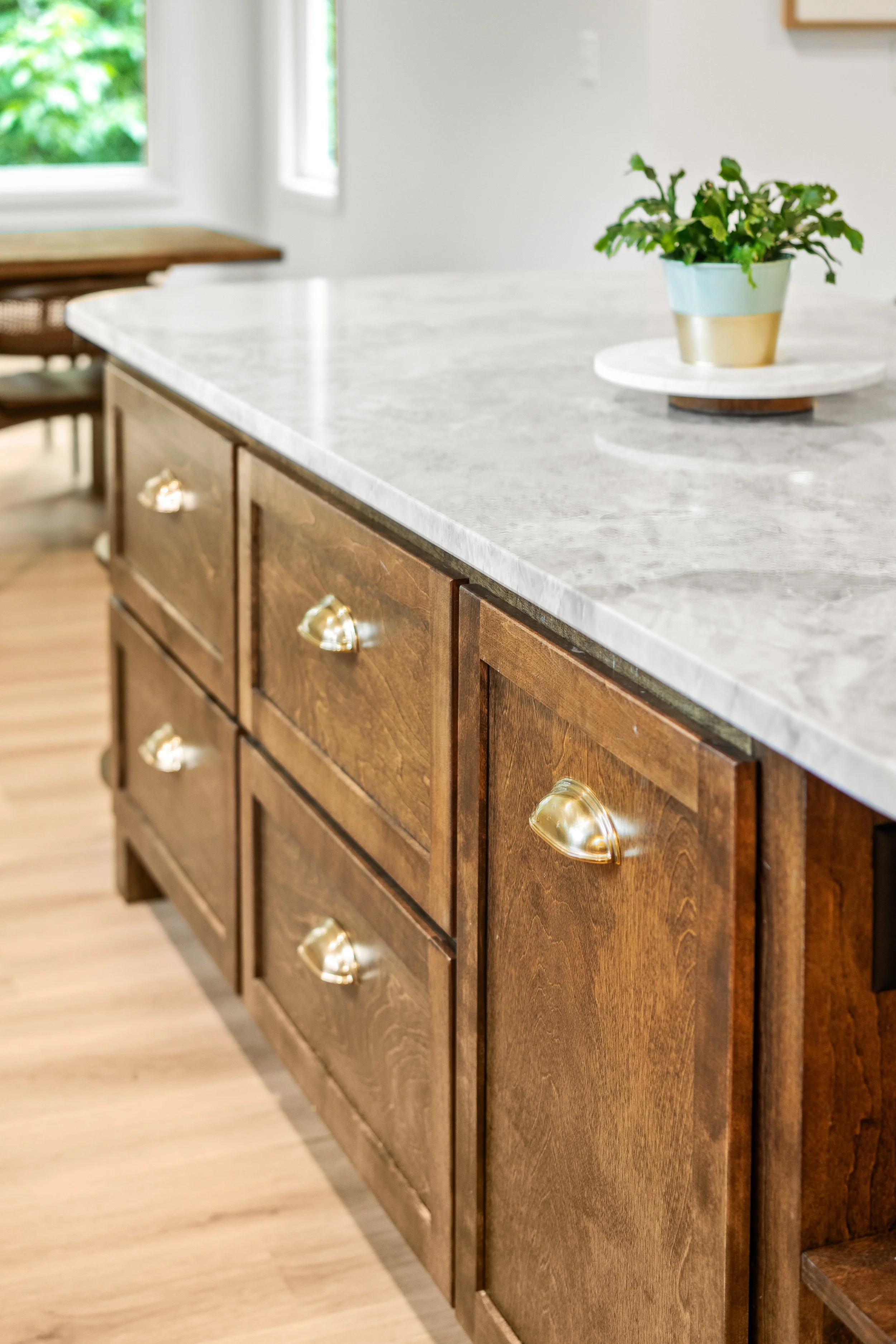 A kitchen island with a marble countertop and wooden cabinets with gold handles, and a small potted plant on top of a white round tray.
