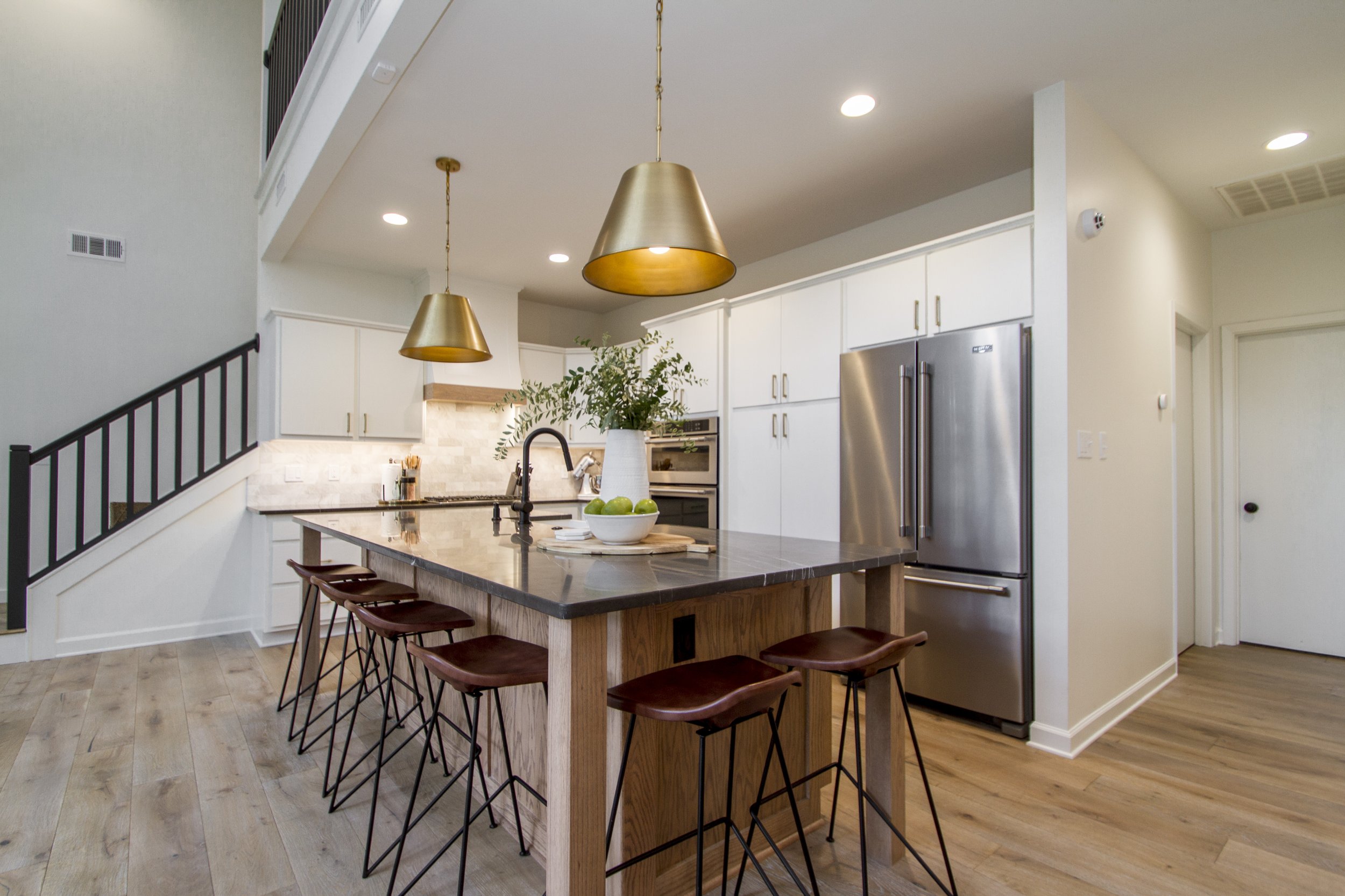 Modern kitchen with a large island, pendant lights, white cabinetry, stainless steel refrigerator, and hardwood floors.