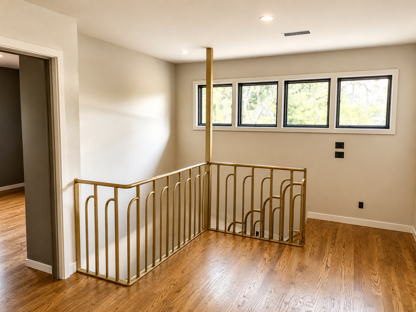 Interior view of a staircase with a wooden railing, overlooking a small landing with four upper windows providing natural light, hardwood flooring, white walls, and ceiling recessed lights.