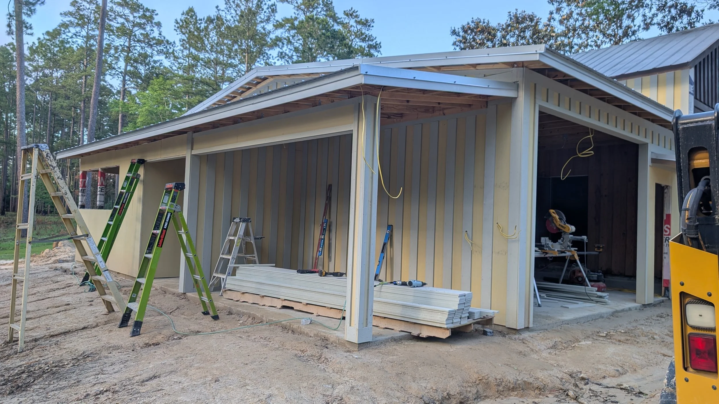 Construction site of a small building with ladders, tools, and building materials, set in a wooded area.