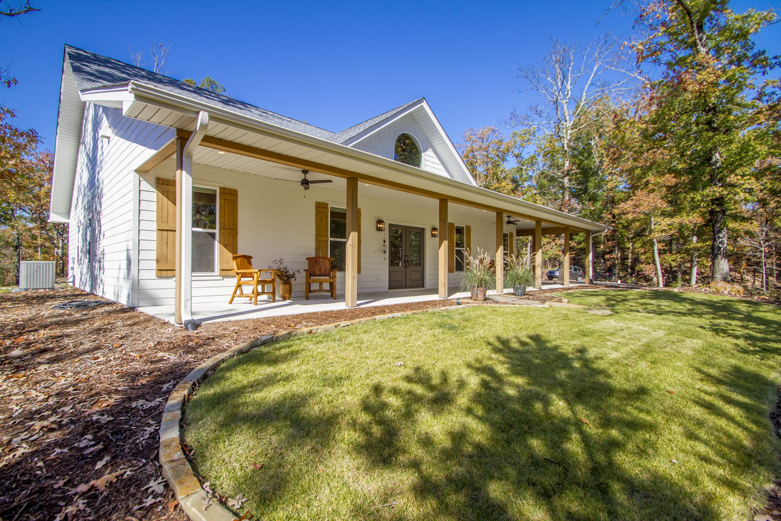 A white house with a front porch, wooden shutters, and a gabled roof, surrounded by trees with fall foliage and a well-maintained lawn.