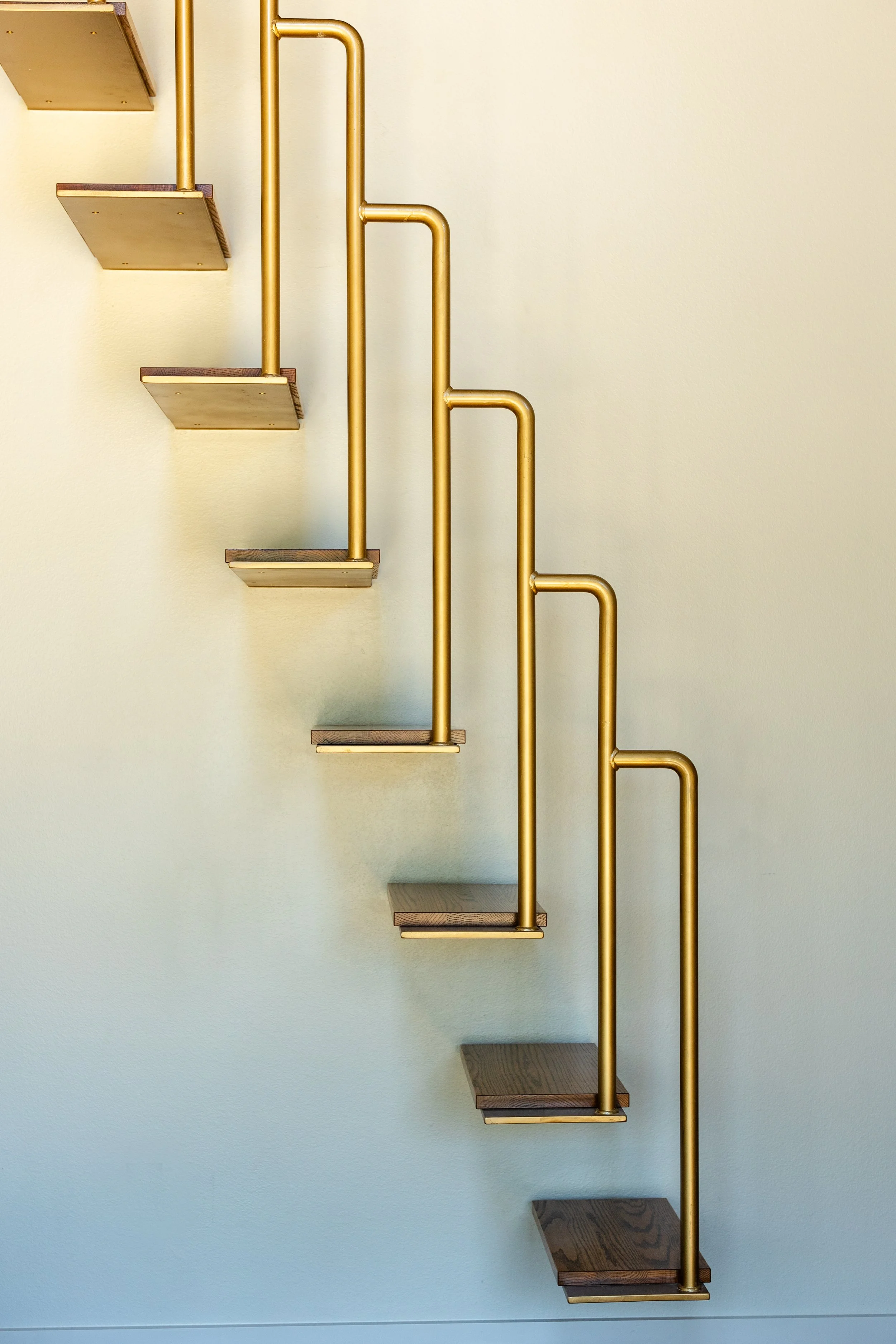 A modern staircase with dark wooden steps and shiny gold railings against a plain light-colored wall.