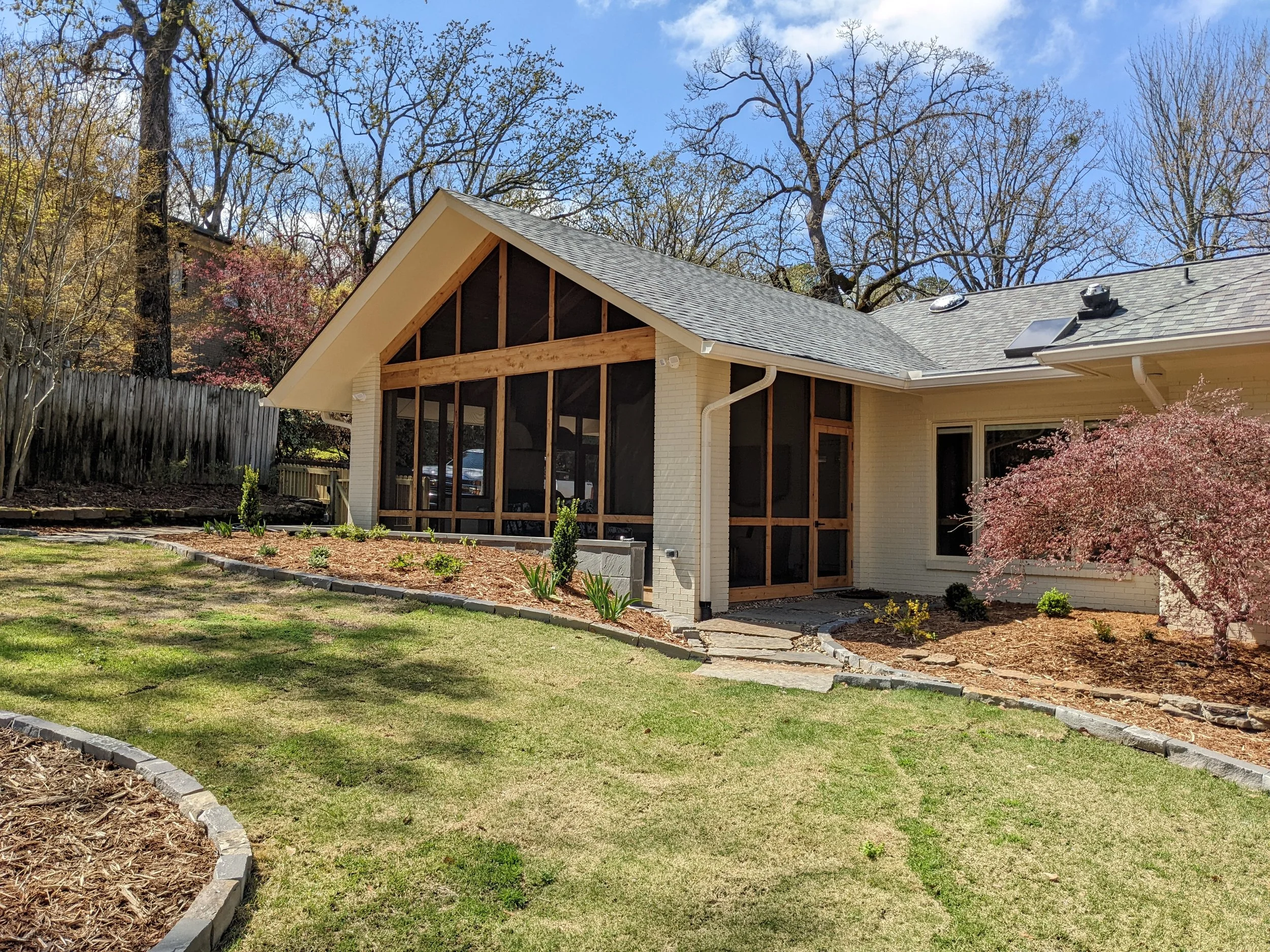 Backyard view of a house with a newly built front porch, surrounded by trees and a well-maintained lawn.