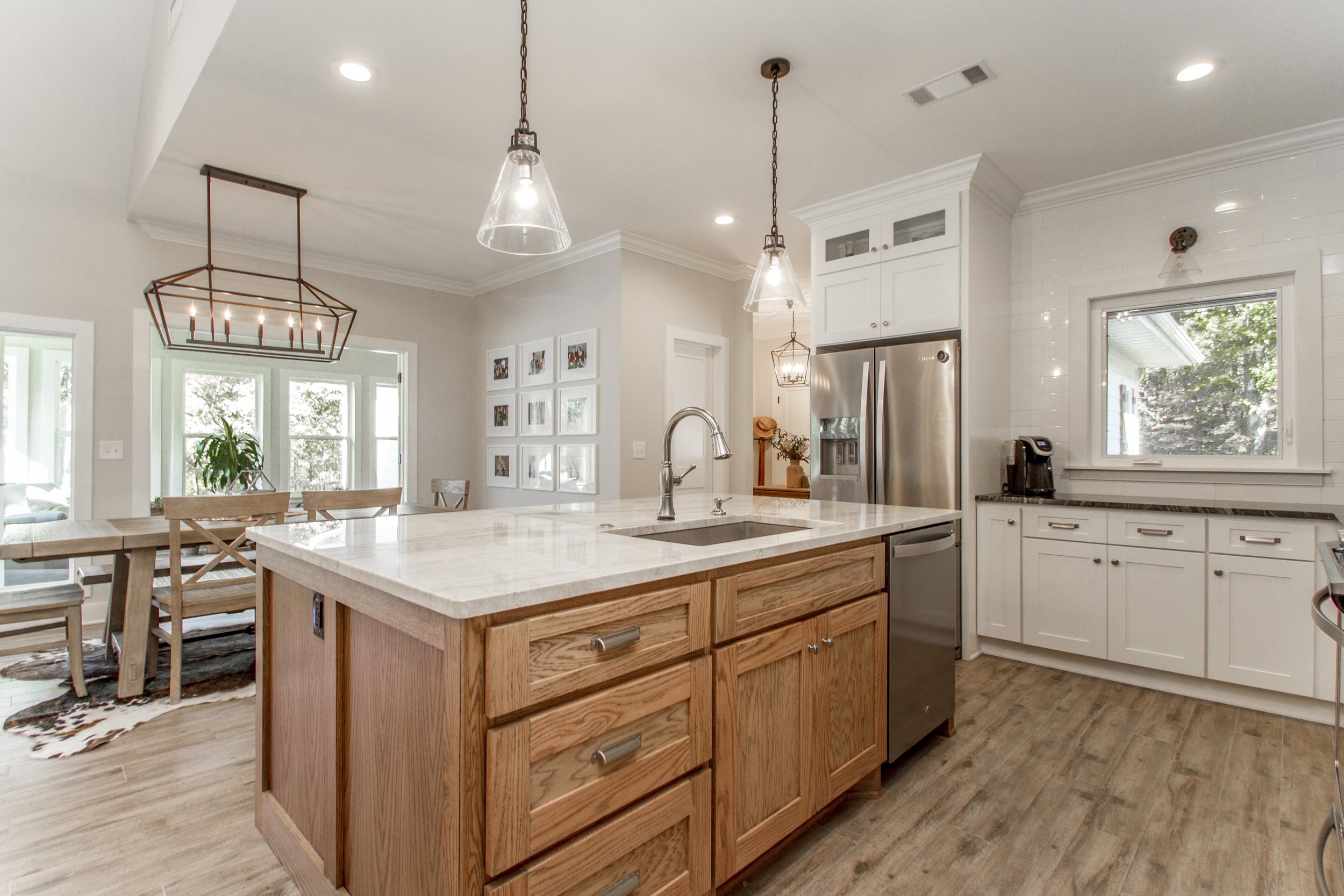 Modern kitchen with white cabinets, stainless steel fridge, marble countertop island, pendant lights, and a window overlooking greenery.