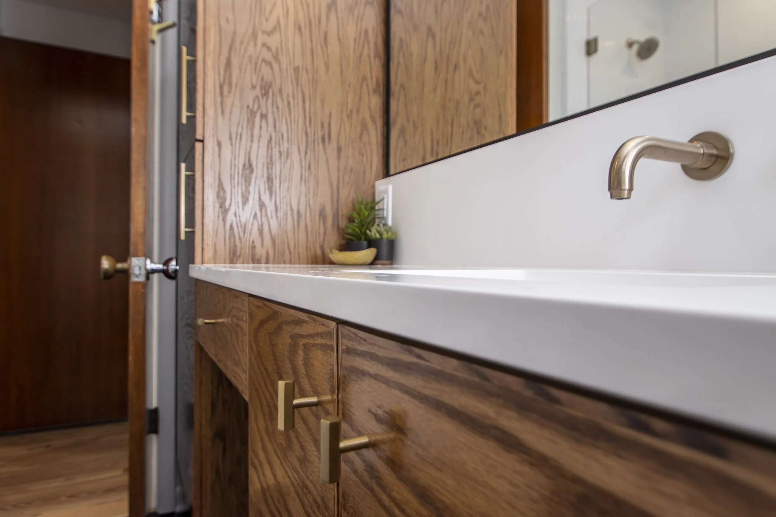 A kitchen with wooden cabinets, a countertop, two potted plants, and a faucet, with a door in the background.