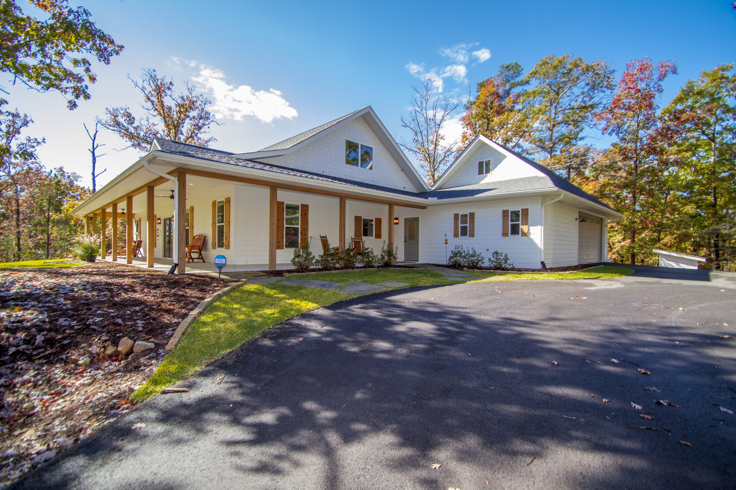 A modern white house with a covered porch, surrounded by fall trees with multicolored leaves, under a blue sky.