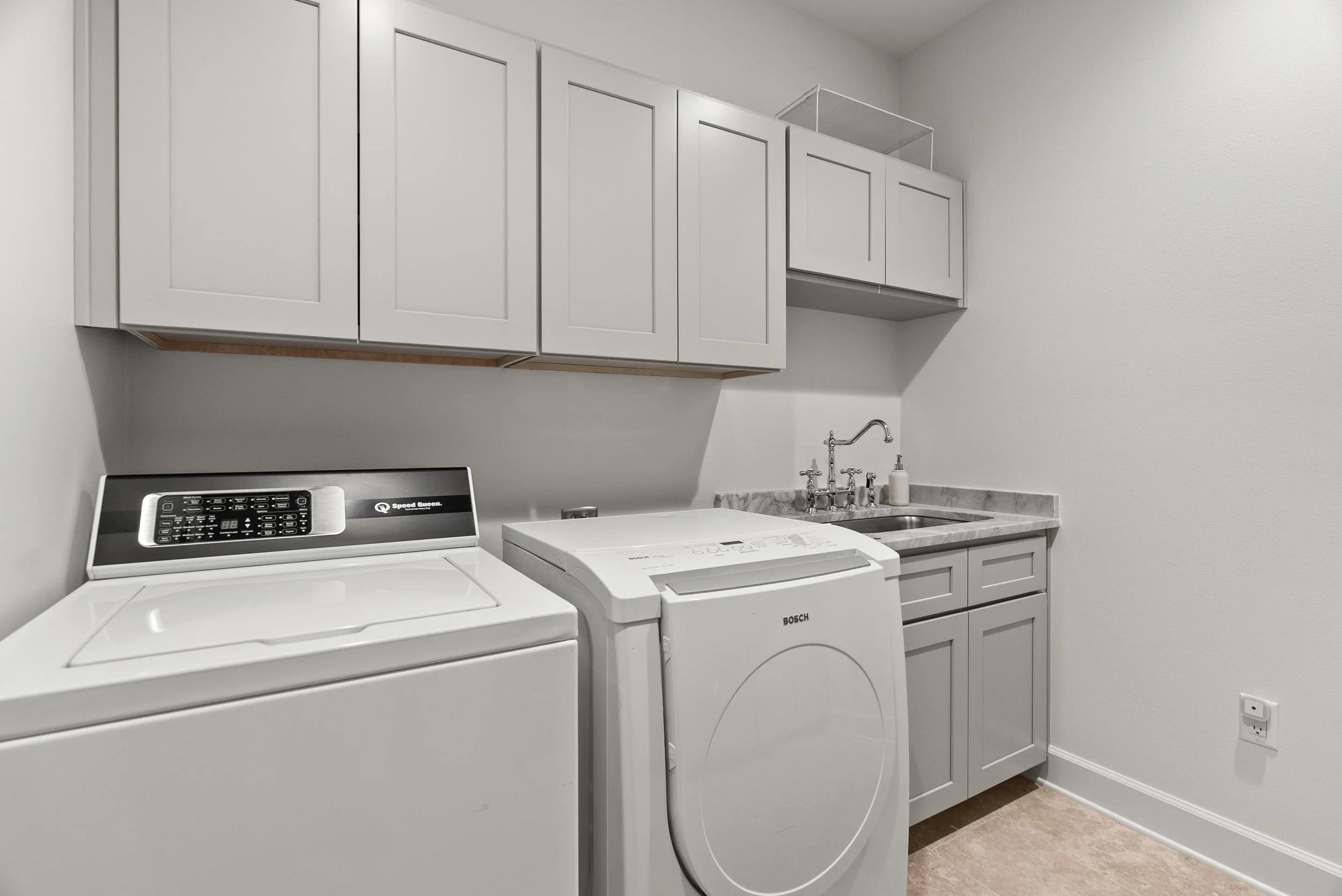 Laundry room with white cabinets, top load washer, front load dryer, marble countertop, sink, and grey walls.