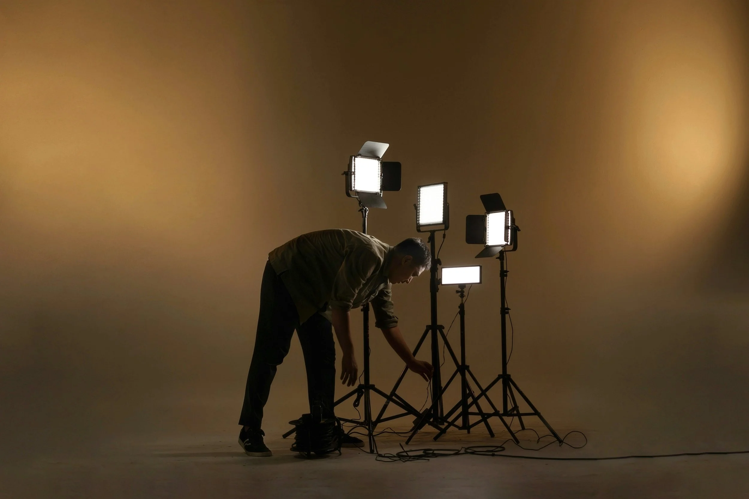 Un homme ajuste des lumières de studio dans une pièce vide avec un fond beige.