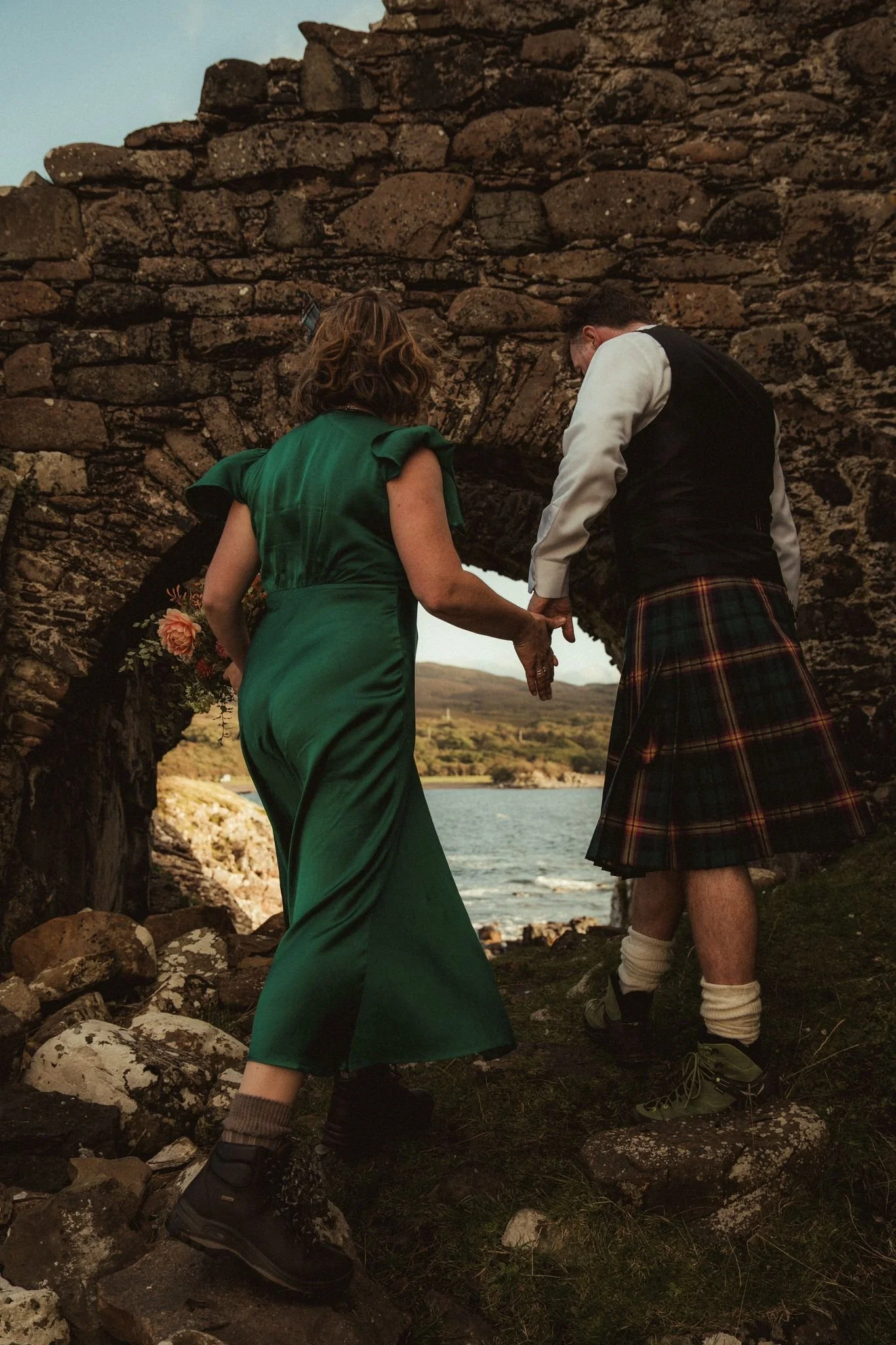 Newlyweds walking through the historic stone archway at Dunscaith Castle on the Isle of Skye after their elopement.