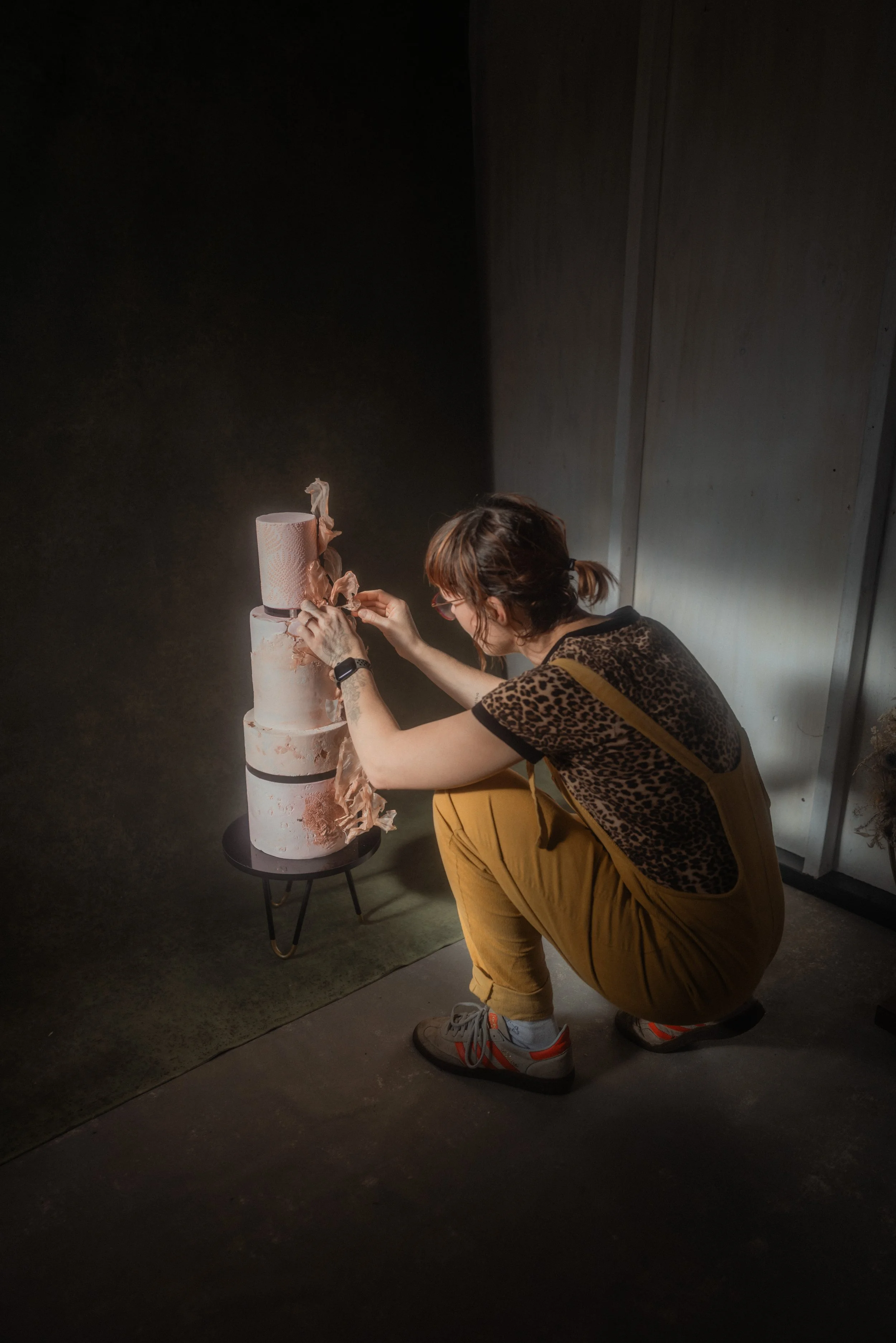 Laura from Wilde Cake Studio carefully arranging handmade rice paper details on a luxury contemporary wedding cake during an editorial photoshoot.