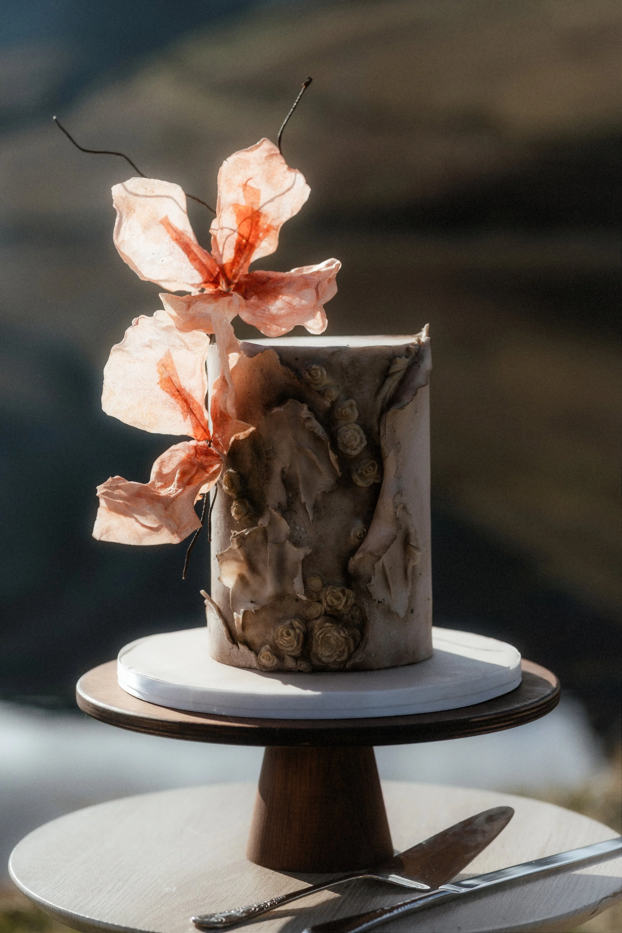 Nature-inspired wedding cake by Wilde Cake Studio with a textured dark finish and handcrafted wafer paper flowers, created on the Isle of Skye for a destination wedding.