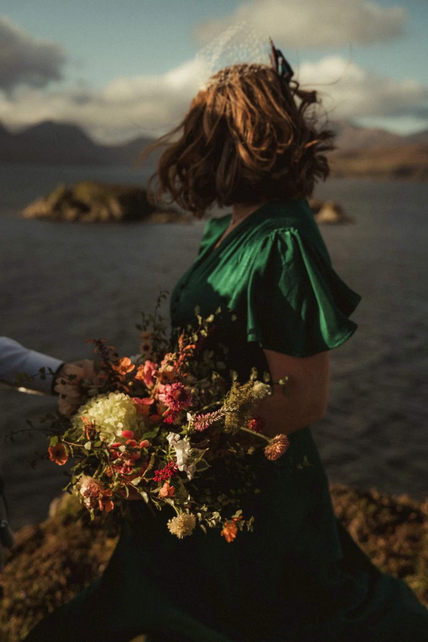 Bride overlooking the sea at Dunscaith Castle on the Isle of Skye, holding a vibrant wedding bouquet.
