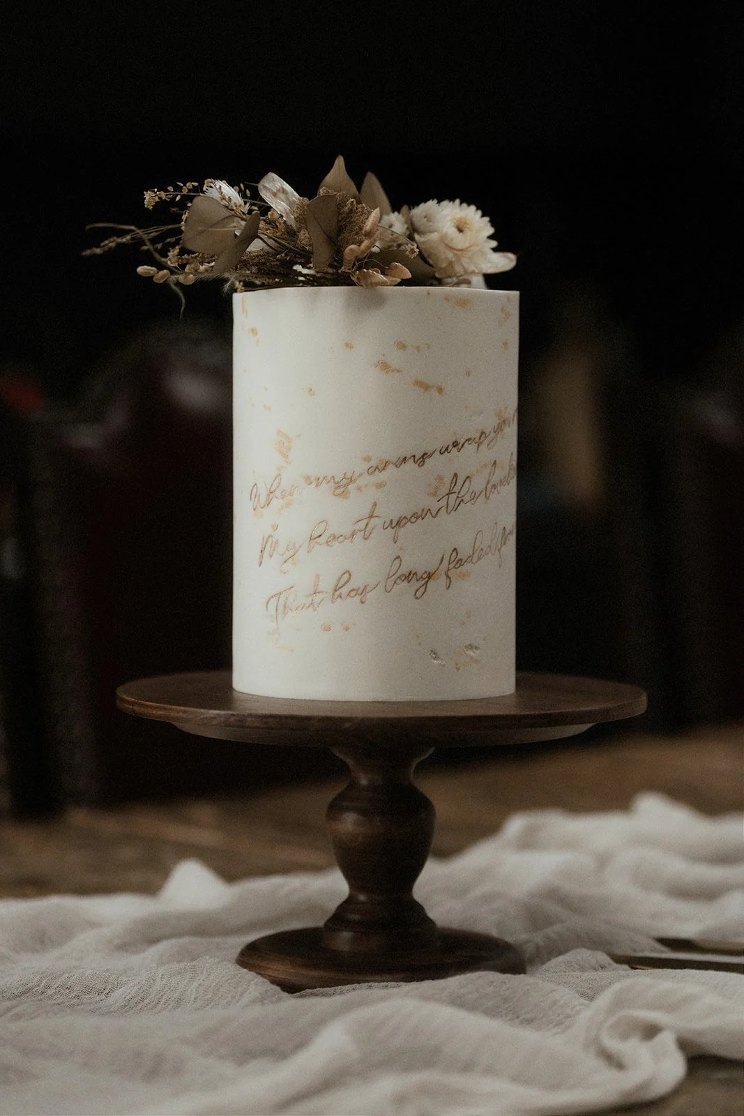 Elegant white contemporary elopement cake with delicate handwritten script, dried flowers and minimalist design displayed on wooden prop options cake stand.