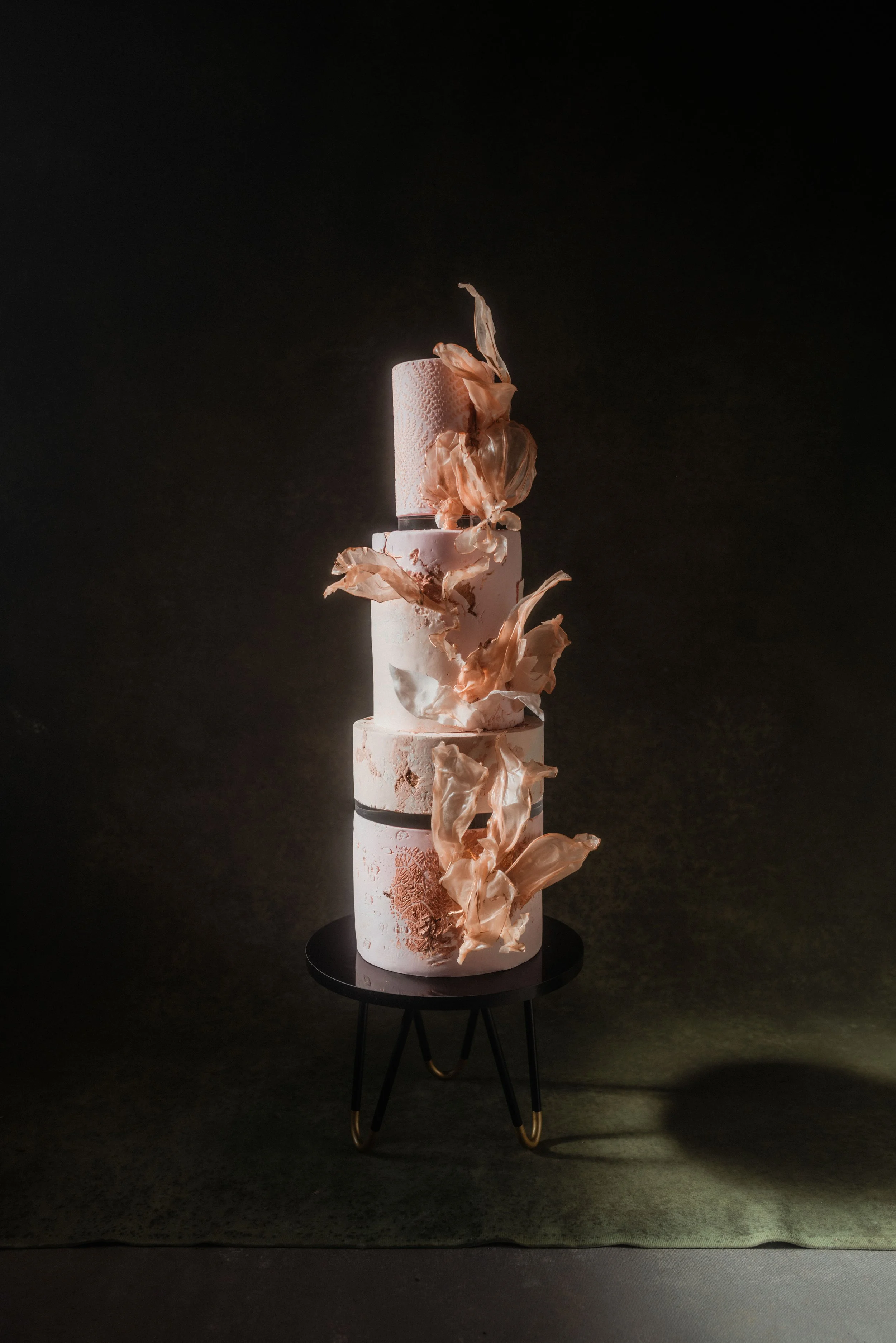 Contemporary four-tier luxury wedding cake with textured finishes, handcrafted rice paper sails and sculptural botanical details, styled for an editorial wedding shoot.