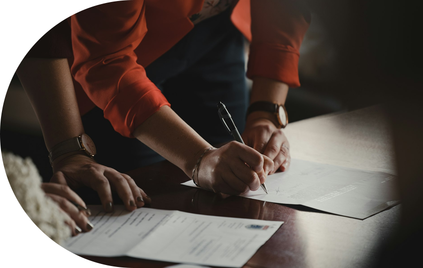 A photograph depicting a person signing a legal document while another person stands next to them.