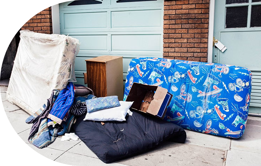 A photograph depicting mattresses, pillows, and indoor furniture thrown out onto a street.