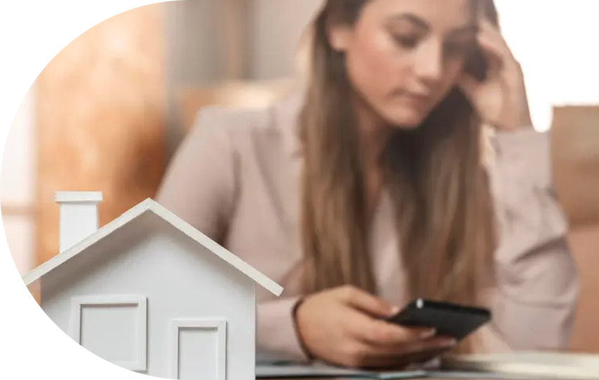 A photograph depicting a miniature-sized house in the foreground and a distressed woman in the background.