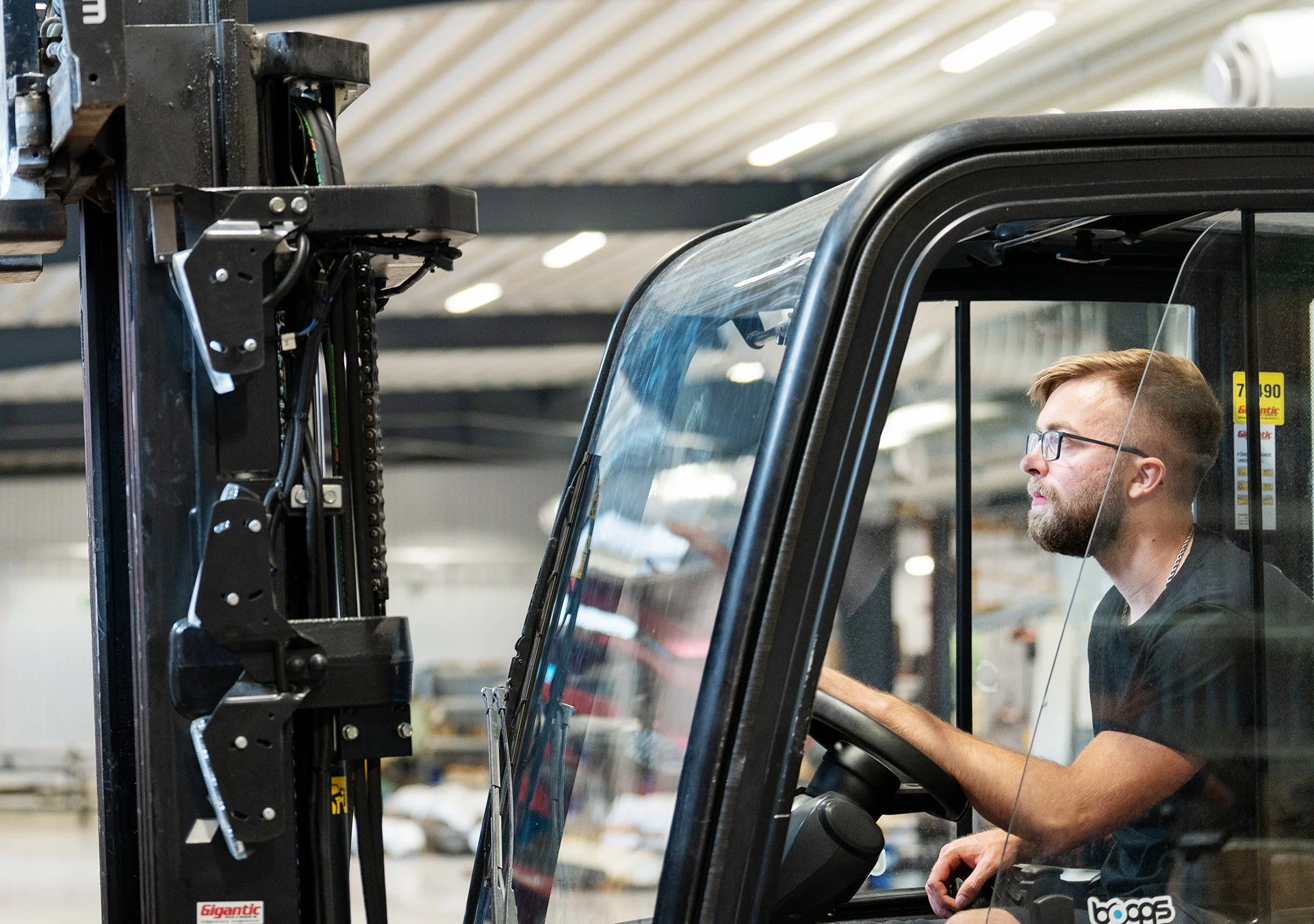 En man med glasögon som sitter i en gaffeltruck i en industrilokal.