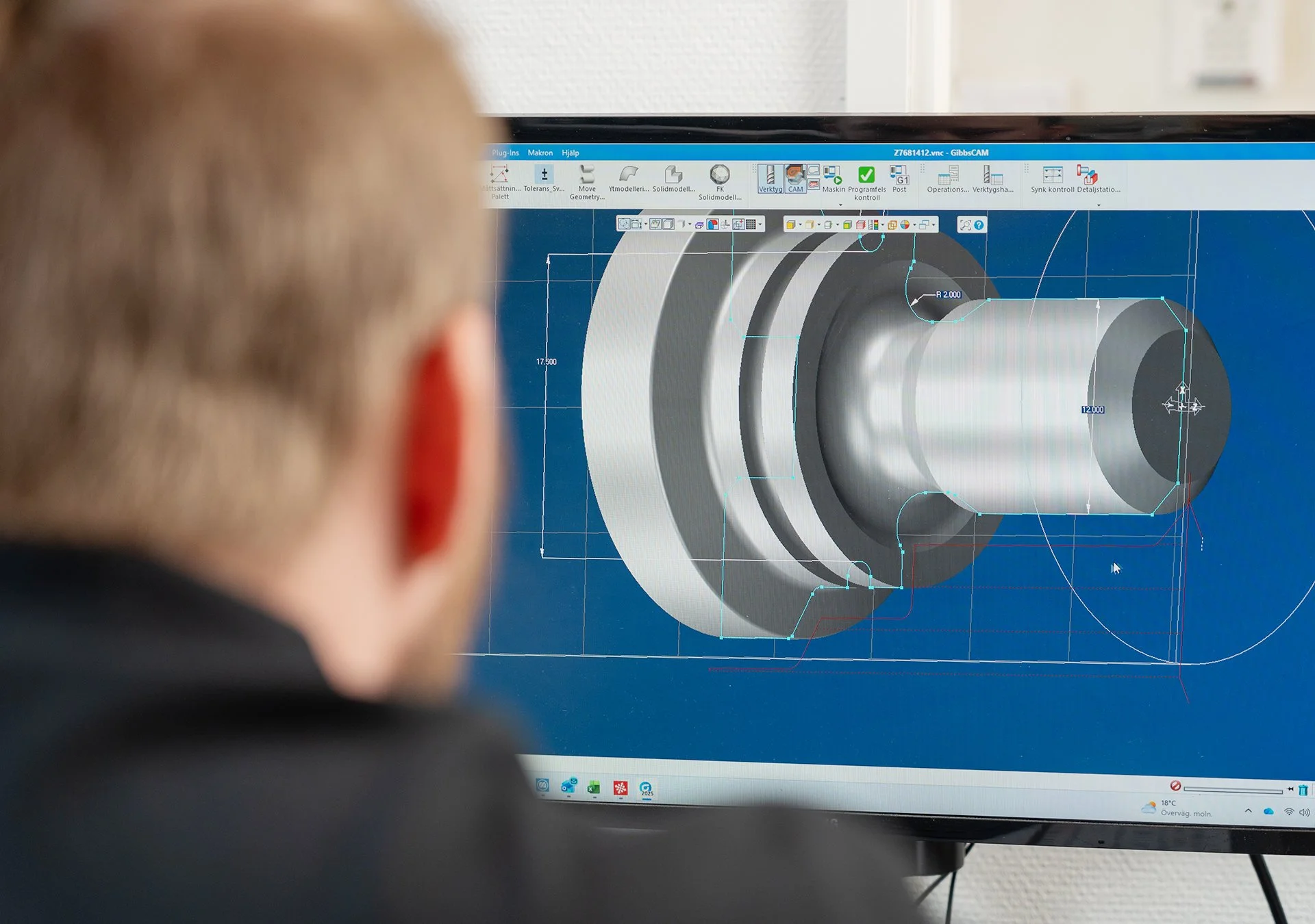 Person som tittar på en datorskärm med en teknikdesign eller CAD-modell av en cylindrisk del.